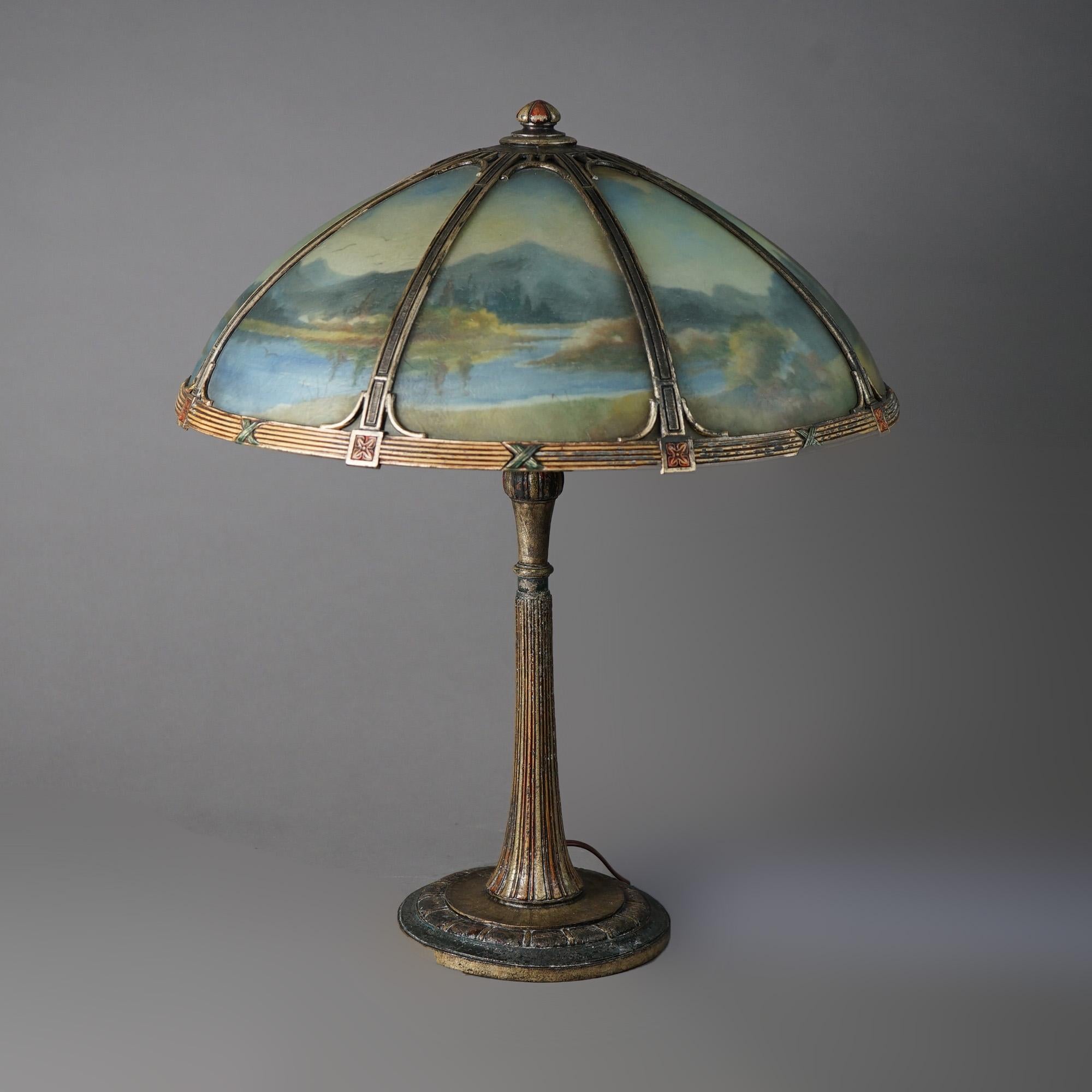 An antique Arts and Crafts table lamp by Bradley and Hubbard offers dome form shade with bent glass panels having reverse painted landscape lake scene over triple socket cast base, c1920

Measures - 23