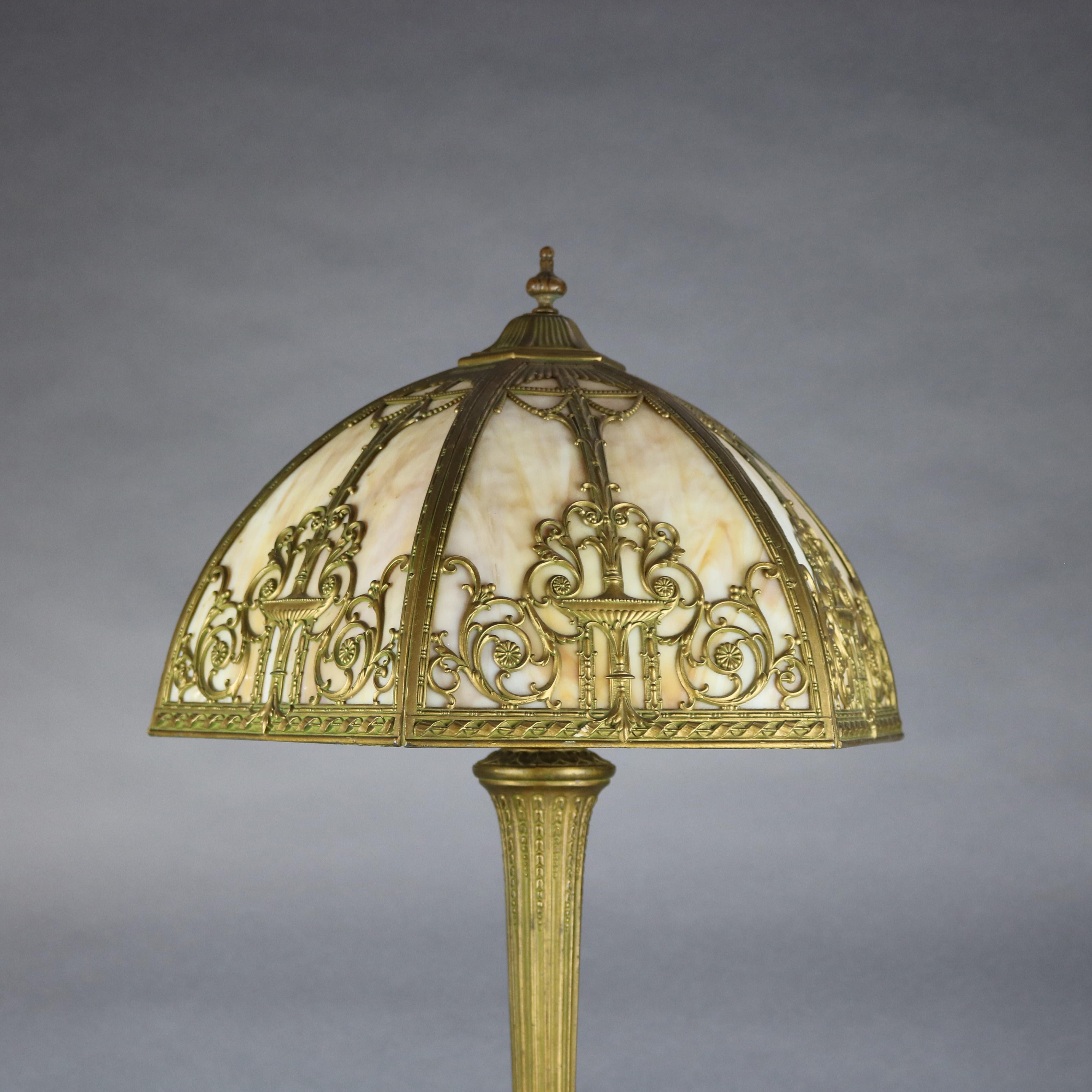 Antique Arts & Crafts table lamp in the manner of Bradley and Hubbard offers neoclassical urn, scrolled foliate and floral filigree cast shade housing bent slag glass panels and surmounting cast double socket base, c1920

Measures: 25
