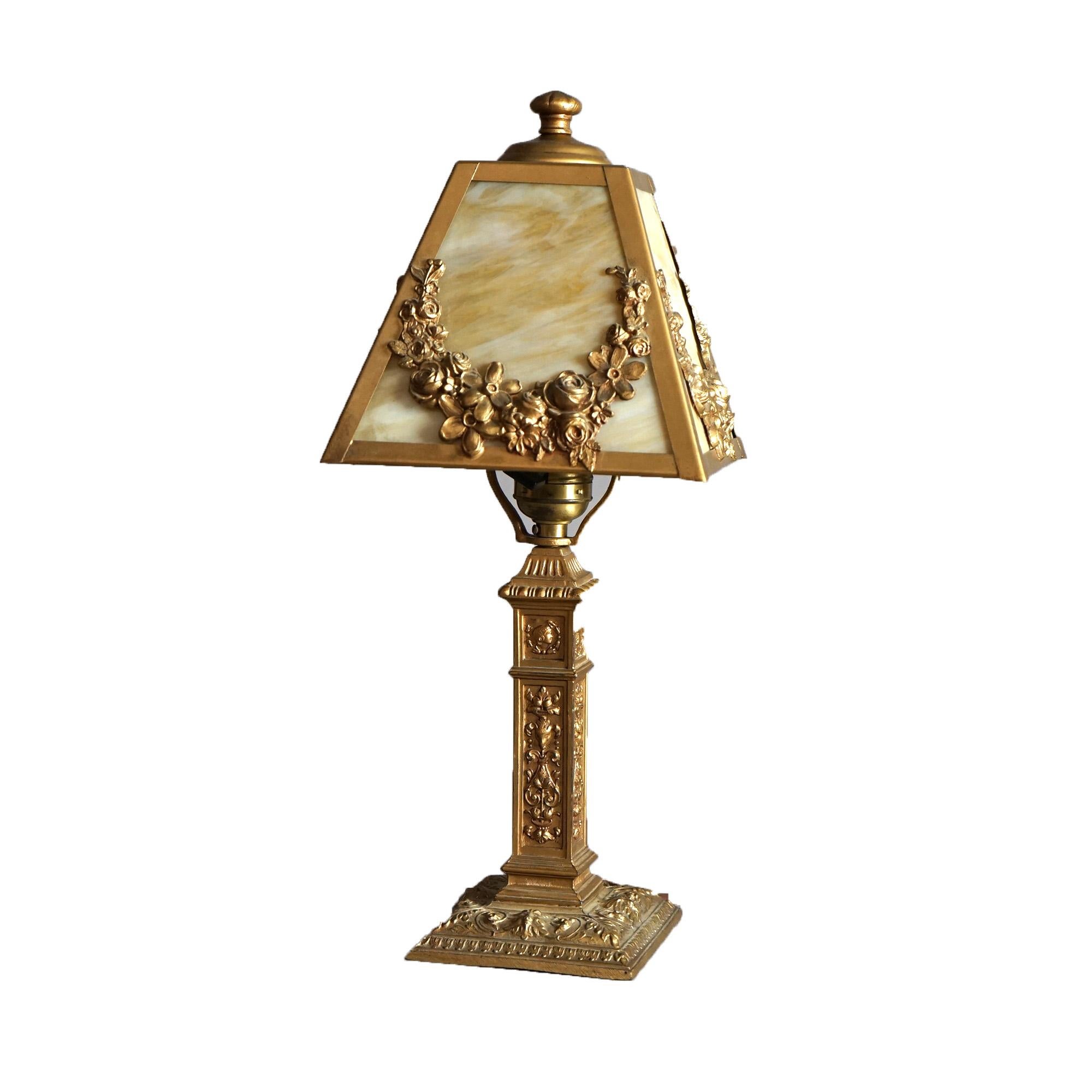 An antique Arts and Crafts boudoir table lamp in the manner of Bradley & Hubbard offers shade with gilt cast metal frame having floral swag elements housing slag glass panels over single socket base, c1910

Measure - 15.5