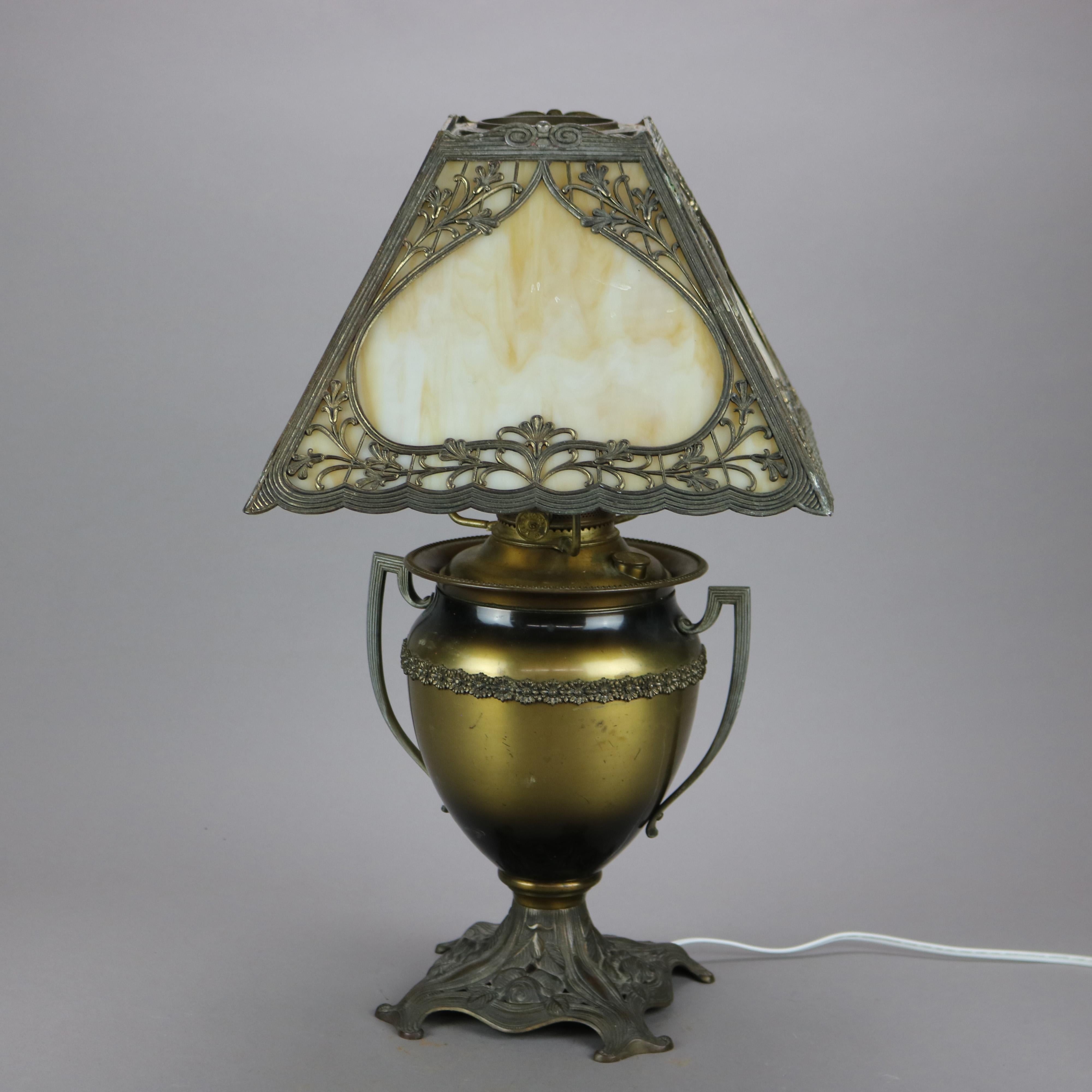 An antique Arts & Crafts table lamp in the manner of Bradley and Hubbard offers filigree shade with inverted heart reserve and housing slag glass panels over single socket urn form oil lamp base with double handles, electrified, c1910.

Measures -
