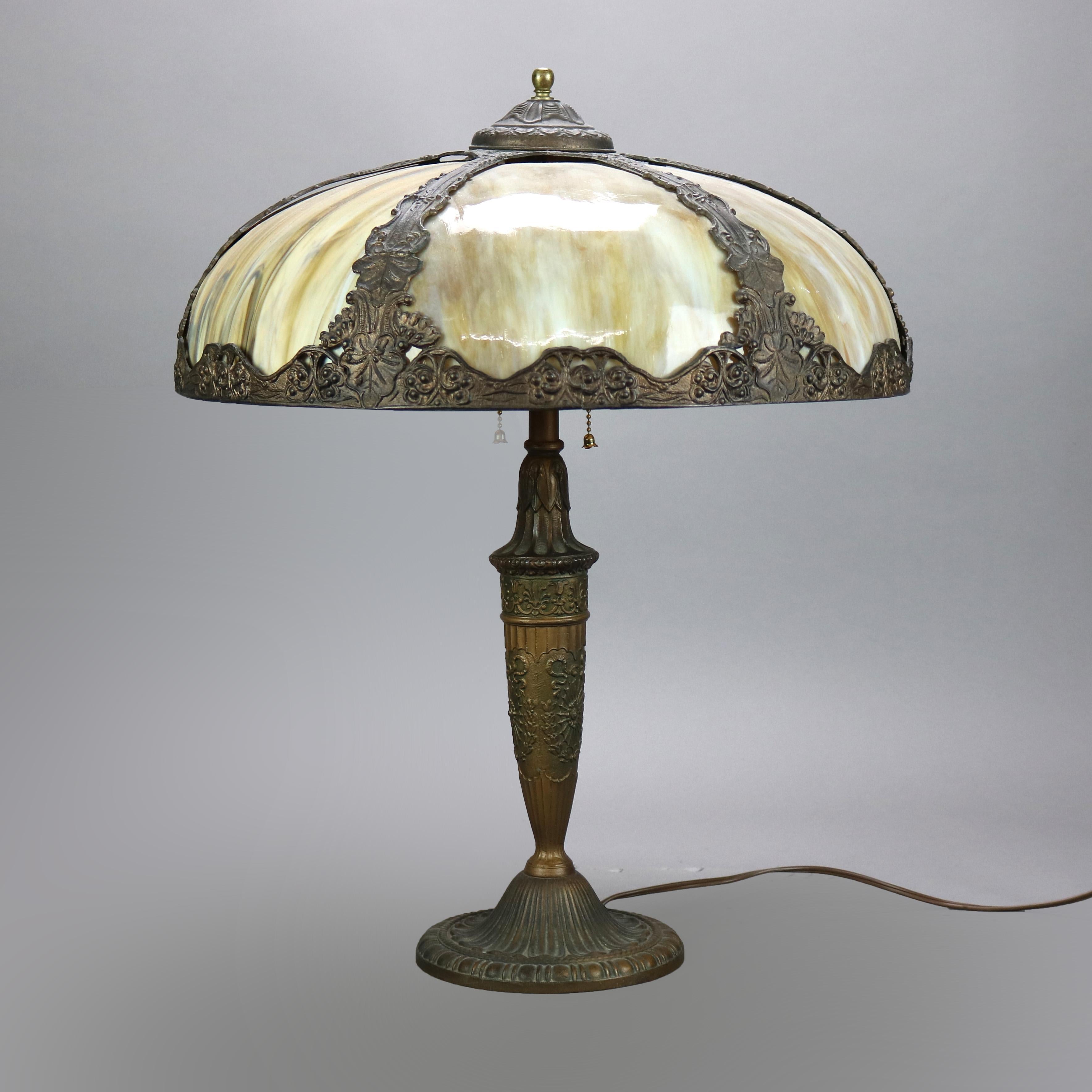 An antique Arts and Crafts table lamp in the manner of Bradley and Hubbard offers cast frame with stylized grape and leaf design and housing bent slag glass panels over cast urn form double socket base, c1920

Measures - 22''H x 18''W x