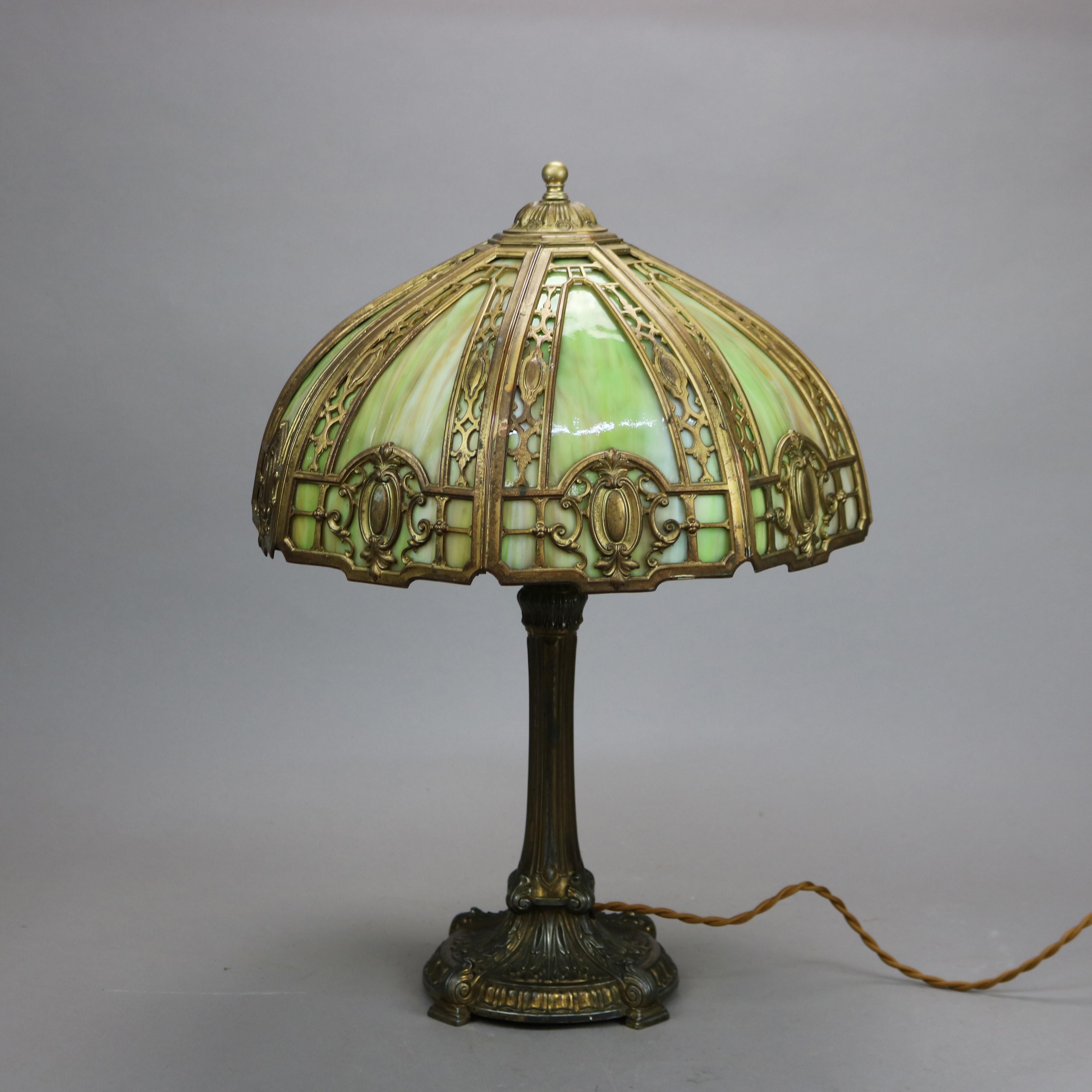 An antique Arts and Crafts table lamp in the manner of Bradley and Hubbard offers cast dome filigree shade with shield form elements and housing bent slag glass panels over double socket cast bas, c1920

Measures - 22''H x 15.25''W x 15.25''D.
