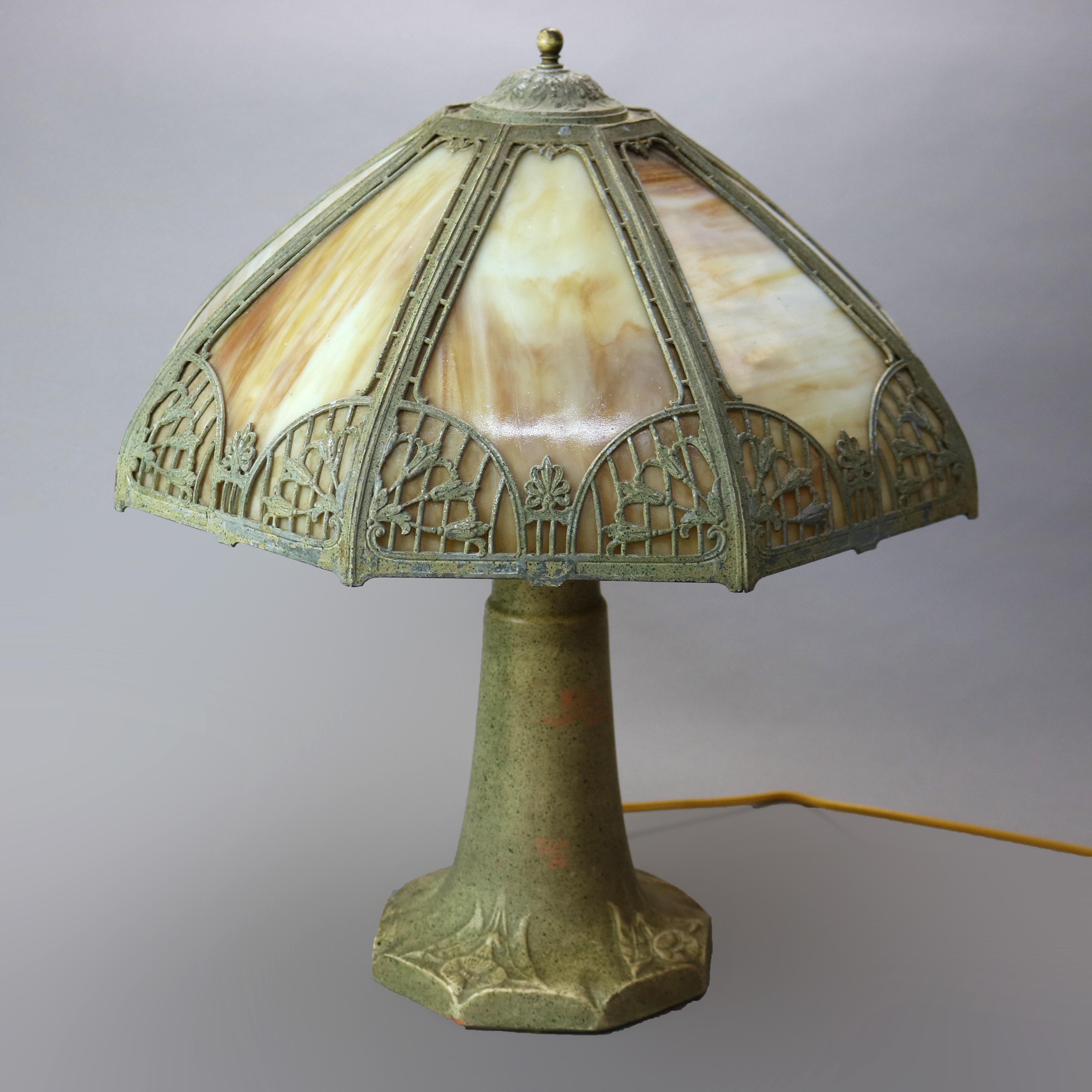 An antique Arts and Crafts table lamp in the manner of Bradley and Hubbard offers cast foliate and floral filigree shade housing bent slag glass panels over double socket terra cotta base with floral elements in relief, c1920

Measures - 21'' H x