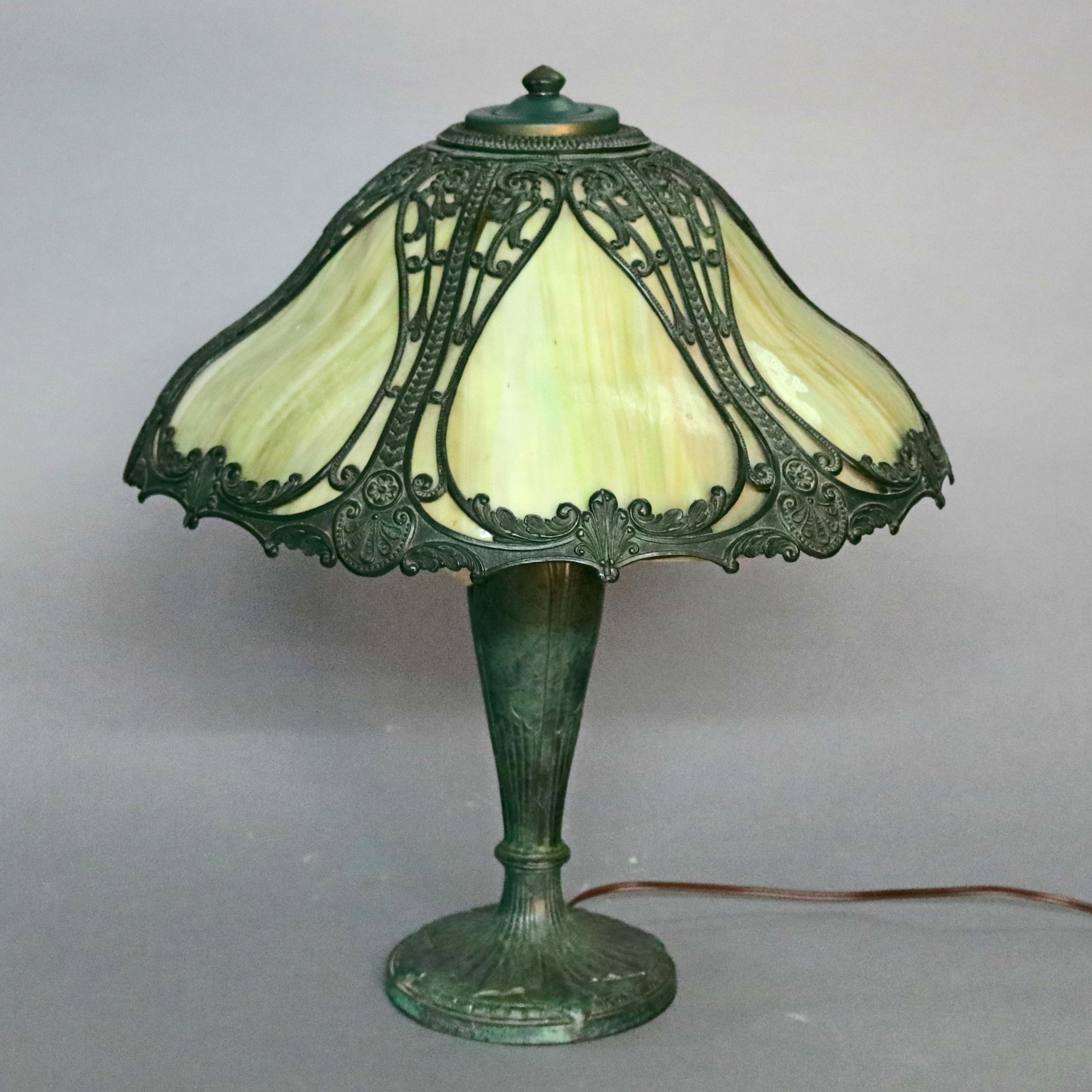 An antique Arts & Crafts Bradley and Hubbard School table lamp offers urn form cast base with two sockets surmounted by six panel bent slag glass shade with filigree cast frame having pierced scroll and foliate design, circa 1920

Measures: 21