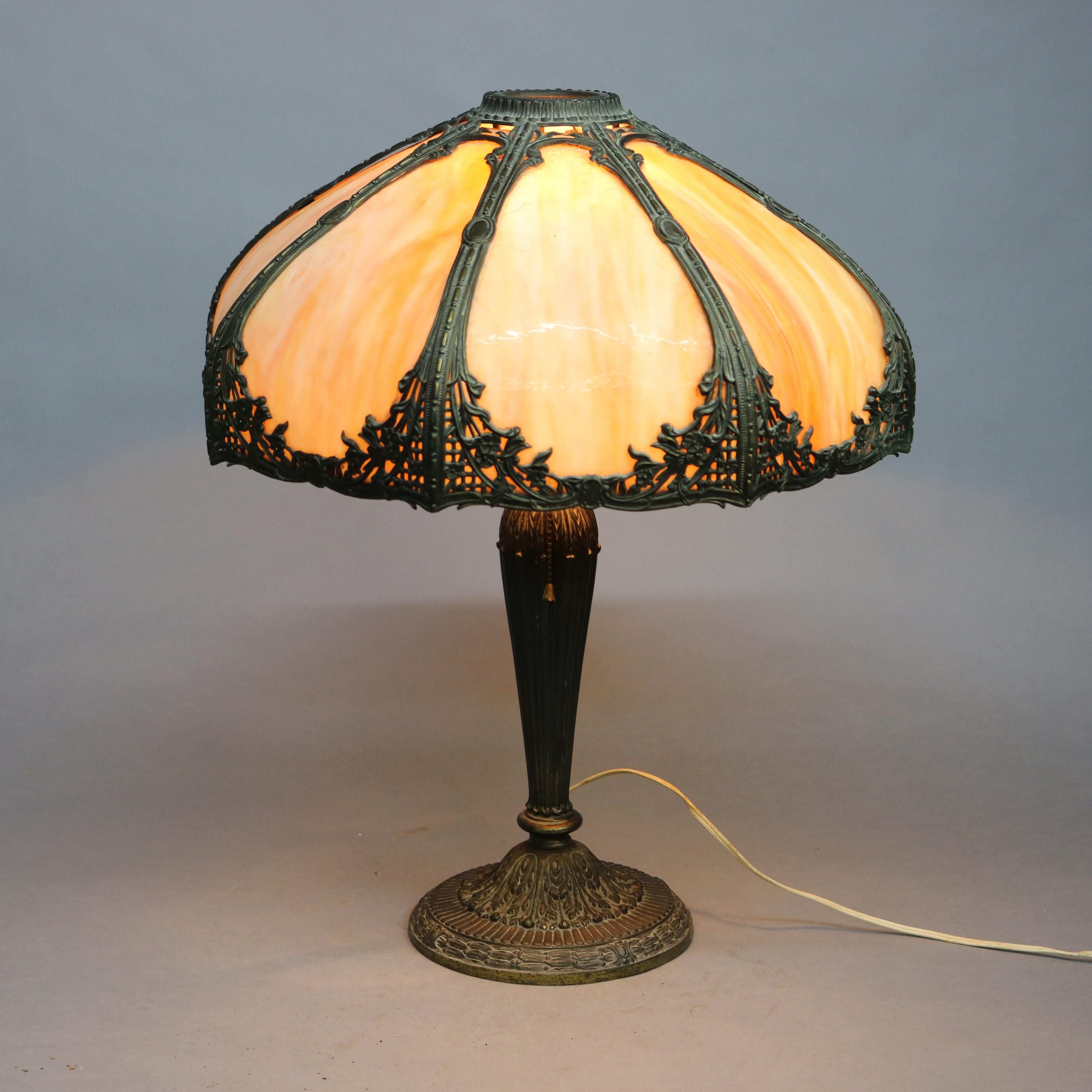 An antique Arts & Crafts table lamp in the manner of Bradley and Hubbard offers foliate cast panel frame housing bent slag glass over single socket base, c1920.

Measures: 23.5