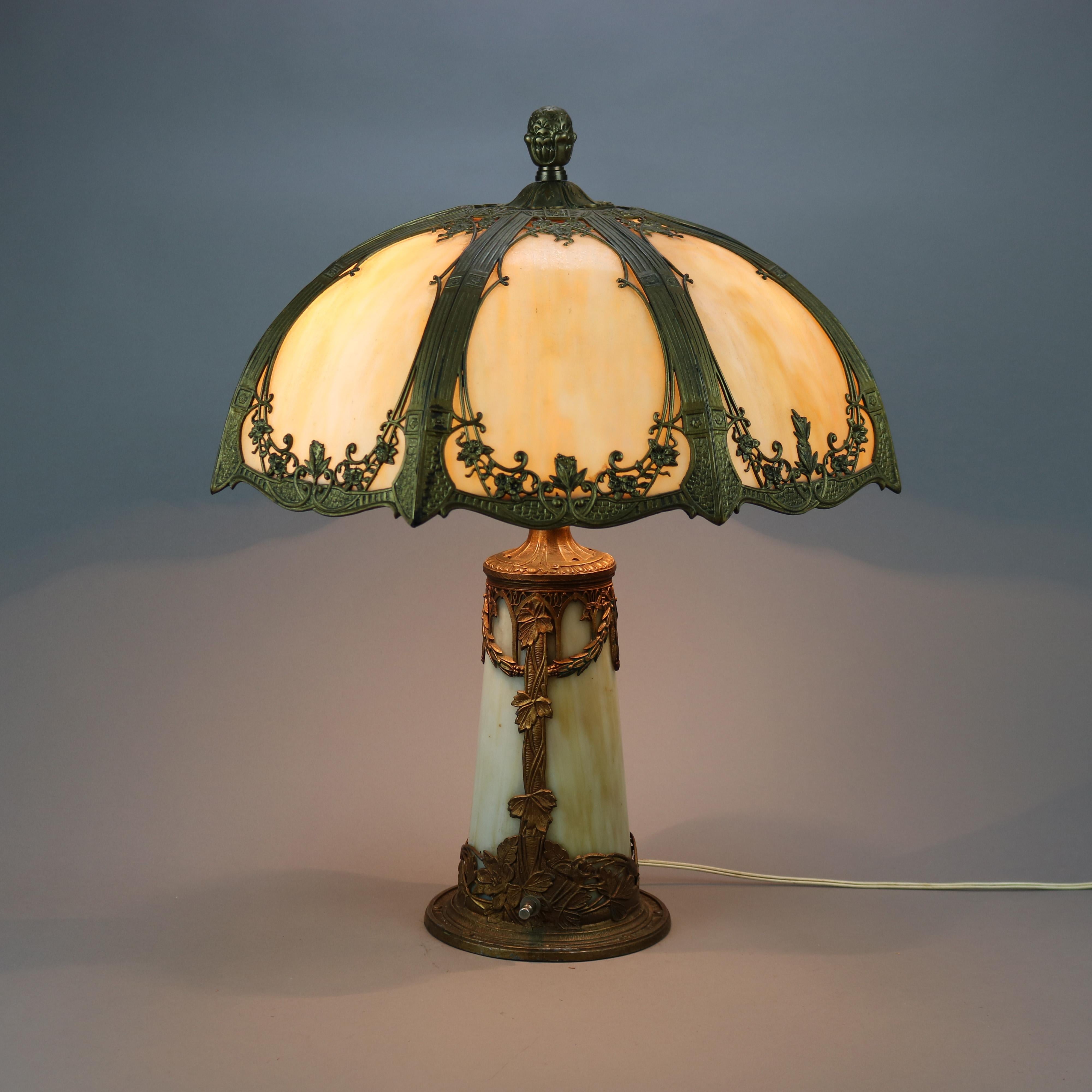 An antique Arts & Crafts table lamp in the manner of Bradley and Hubbard offers shade with filigree foliate, scroll and floral cast shade housing bent slag glass panels over double socket slag glass base, c1920

Measures - 23''h x 19''w x