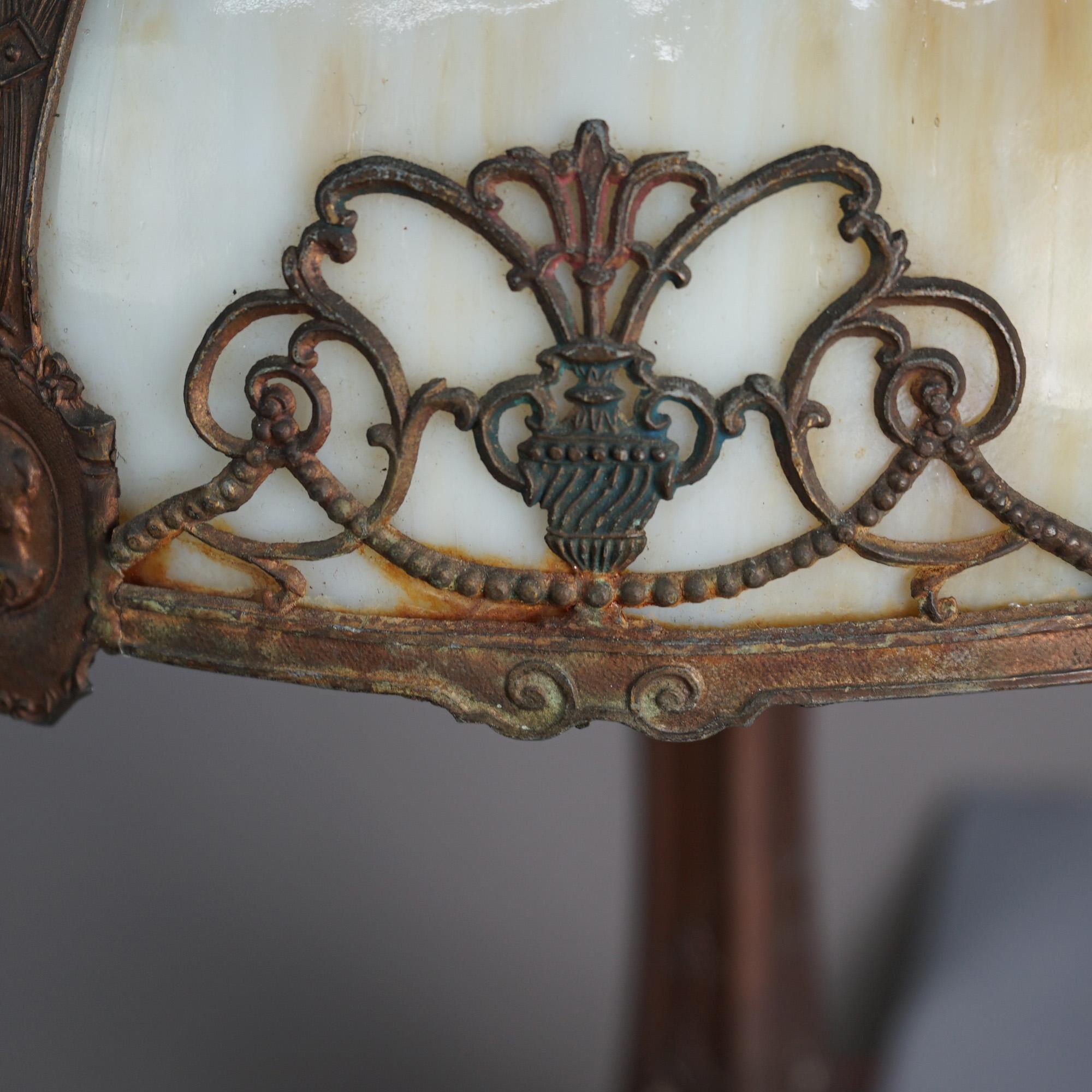 An antique Arts & Crafts table lamp in the manner of Bradley & Hubbard offers dome form shade with cast frame having filigree Classical elements and embossed portrait medallions, housing bent slag glass panels over double socket flared base with