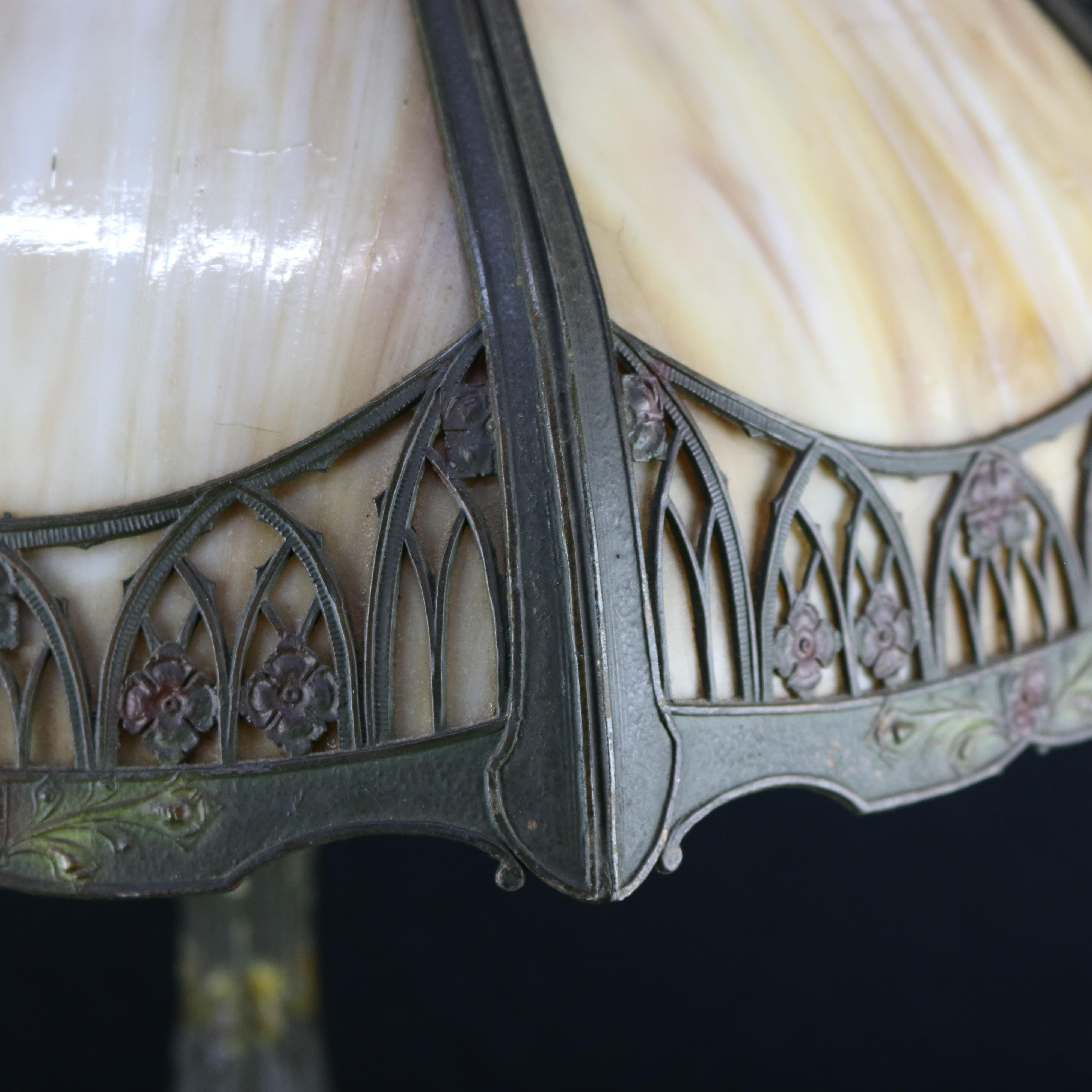 An antique Arts & Crafts table lamp in the manner of Bradley & Hubbard offers slag glass paneled shade with filigree shade having repeating Gothic arch border, surmounting dual light cast base, circa 1910.

Measures: 22.5