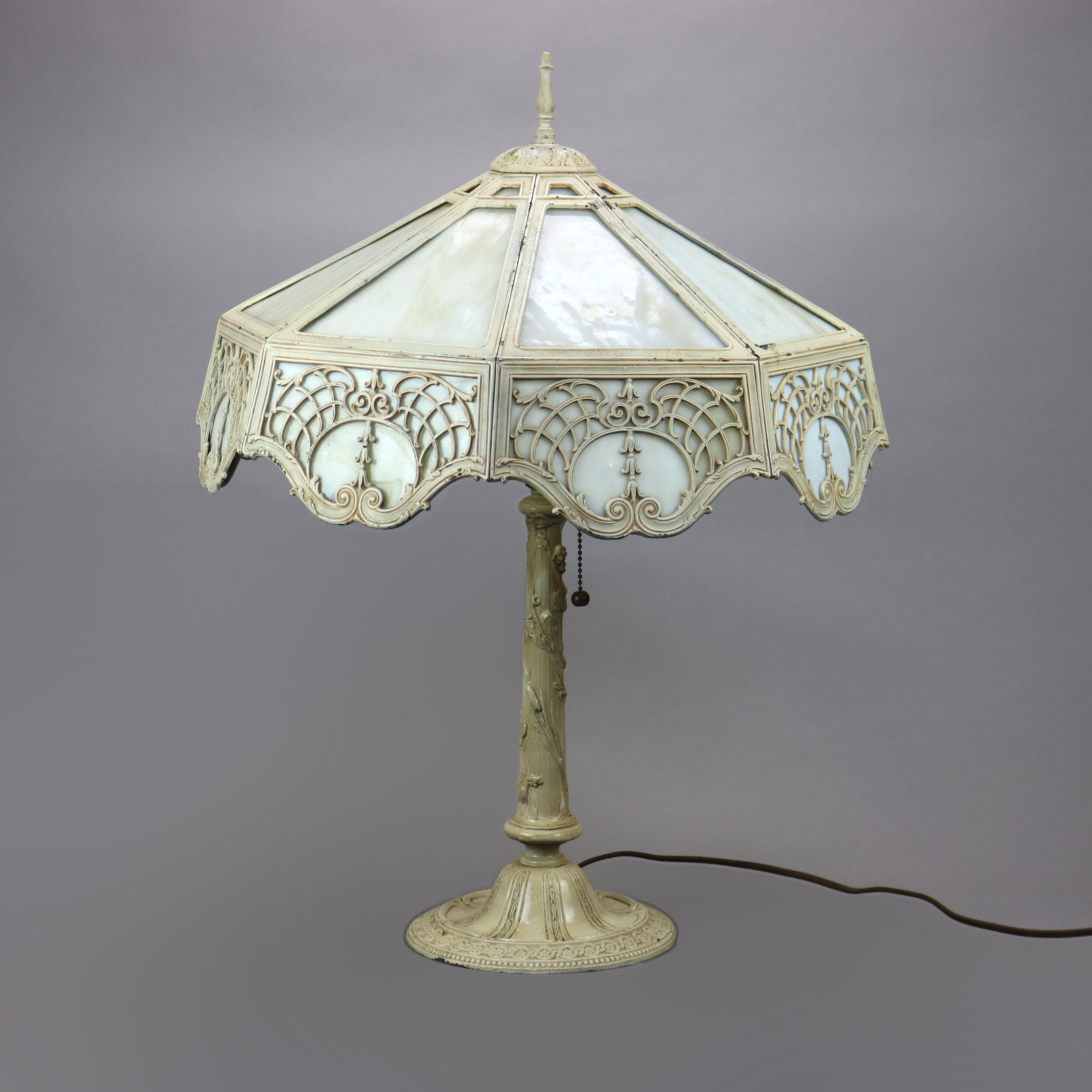 An antique Arts & Crafts table lamp in the manner of Bradley and Hubbard offers cast filigree shade with inverted bellflower and scrolled foliate elements housing slag glass panels over single socket base having foliate elements, c1920

Measures -