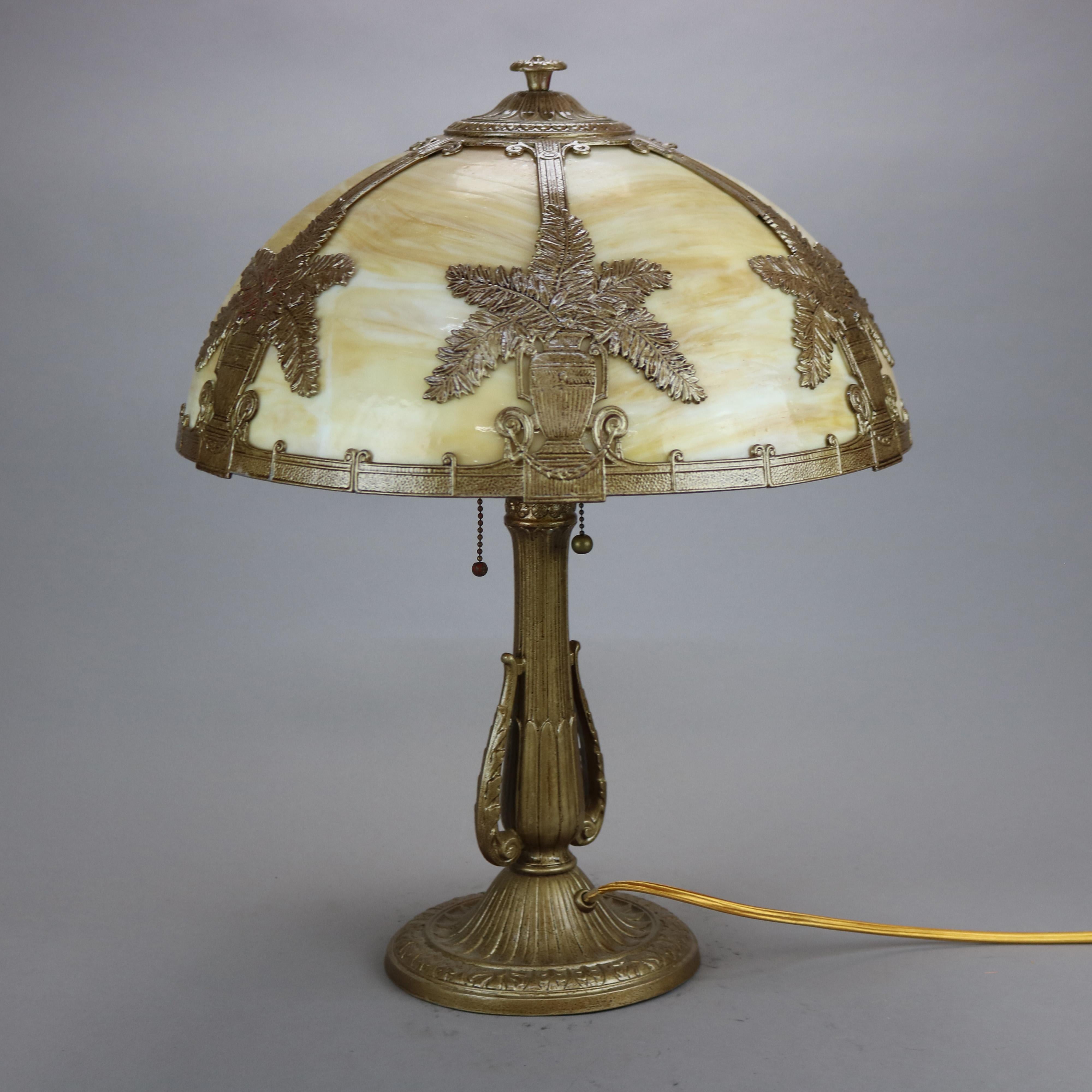 An antique Arts & Crafts table lamp in the manner of Bradley and Hubbard offers dome form shade with cast foliate urn pattern and housing bent slag glass panels over double socket cast base, c1920

Measures - 22.25'' H x 17.25'' W x 17.25''