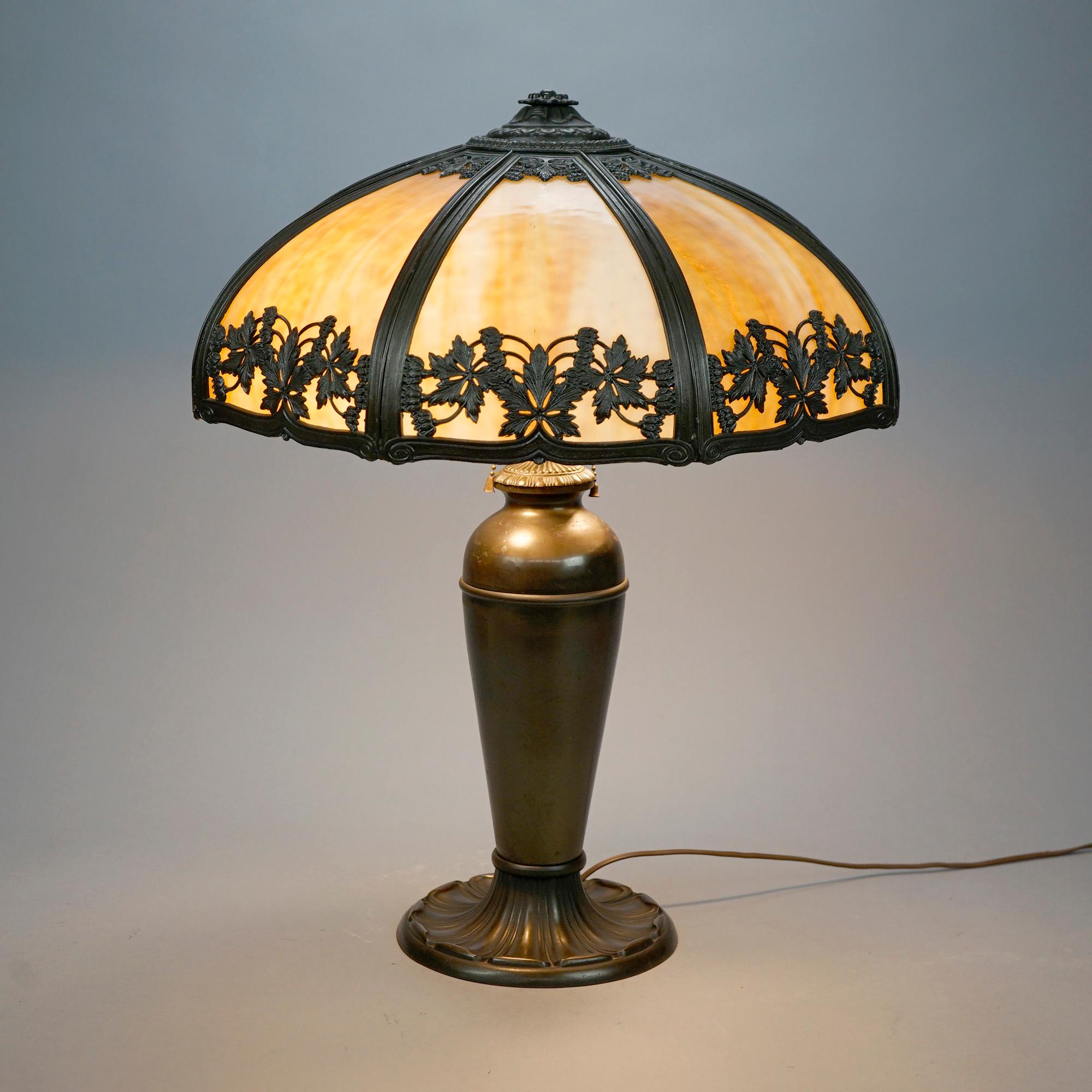 An antique Arts and Crafts table lamp in the manner of Bradley and Hubbard offers dome form cast filigree shade having foliate band and housing bent slag glass panels, over double socket urn form base, c1920
 
Measures- 24'' H x 19'' W x 19'' D.