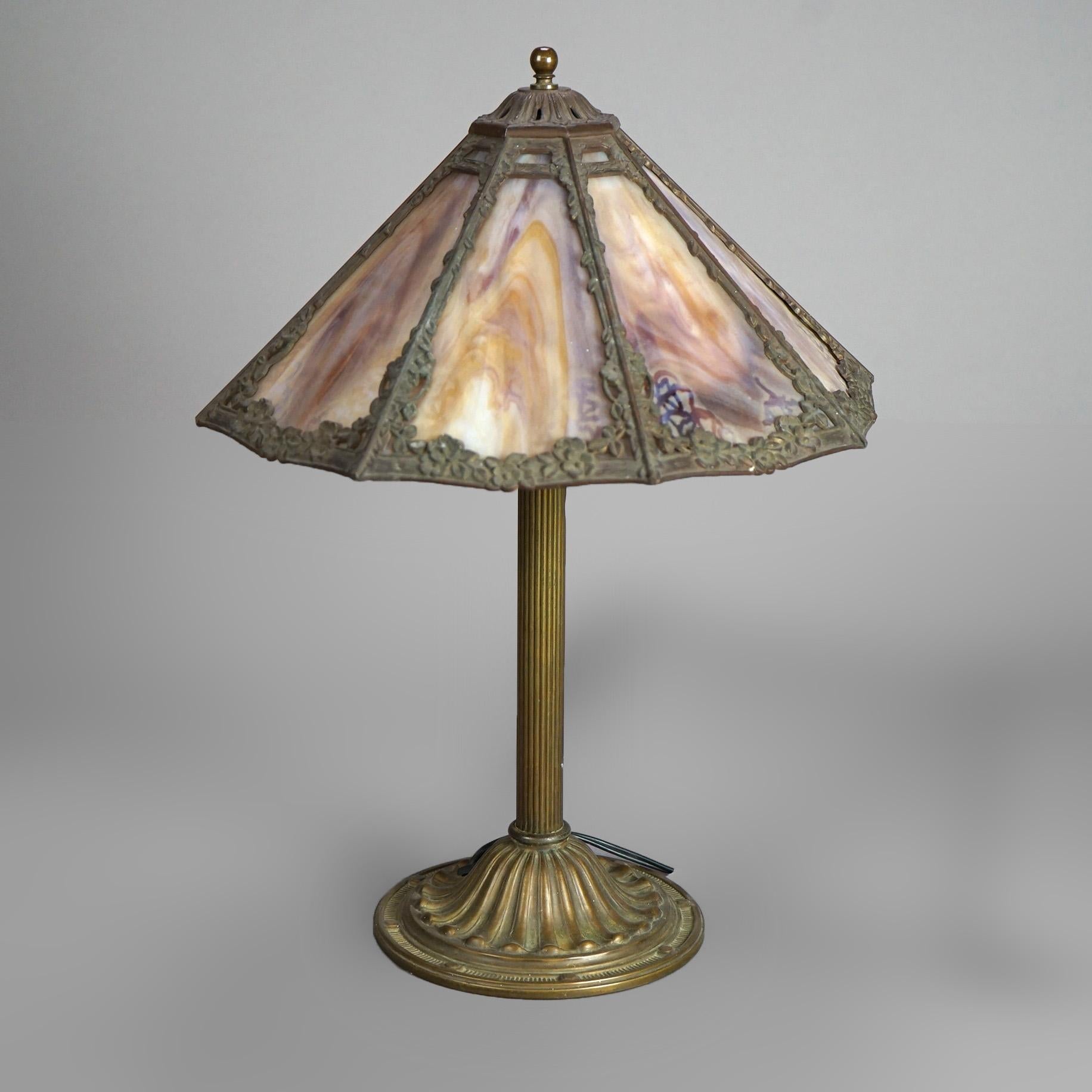 An antique Arts and Crafts table lamp in the manner of Bradley & Hubbard offers foliate cast shade housing slag glass panels over double socket base, c1920

Measures- 19''H x 13.25''W x 13.25''D