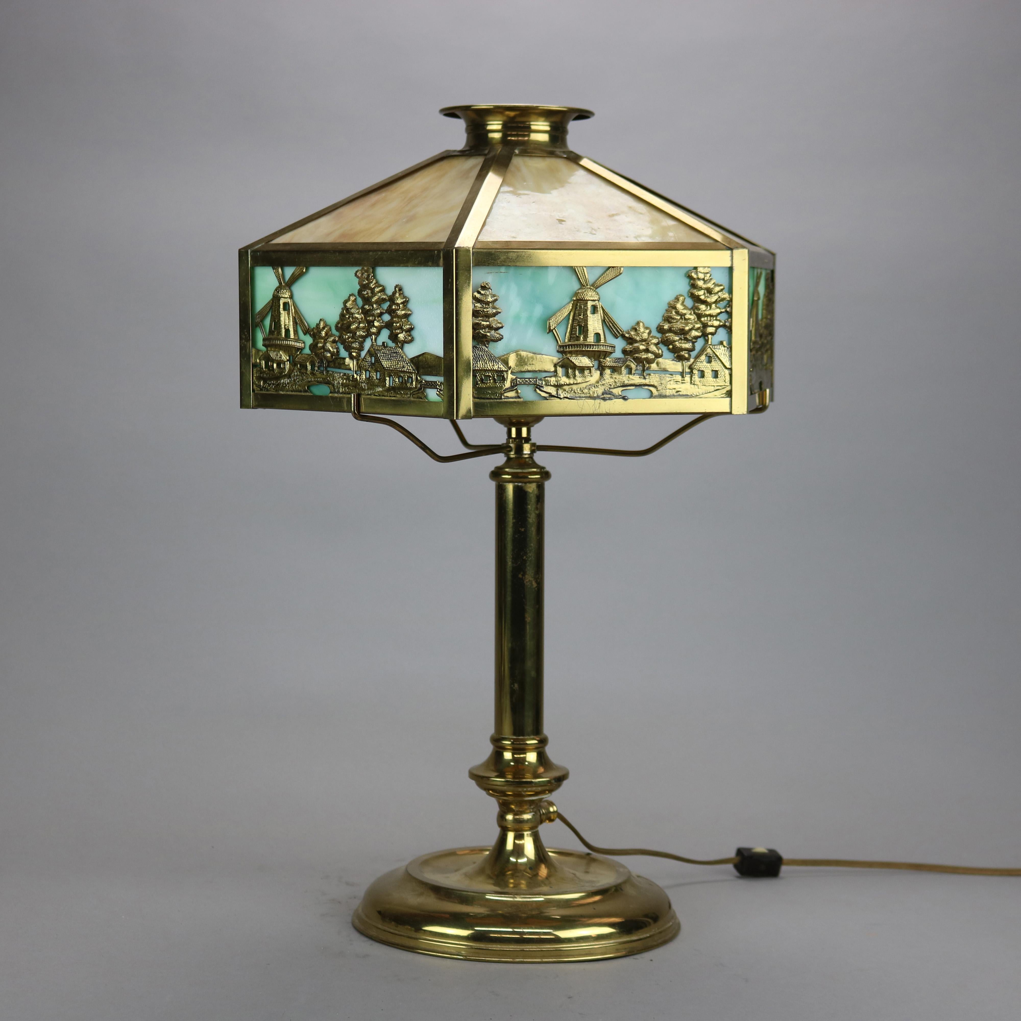An antique Arts & Crafts table lamp in the manner of Bradley and Hubbard offers scenic shade with windmill landscape frame housing two tone slag glass over single socket cast base c1920

Measures - 20.75''H X 12.25''W X 12.25''D.