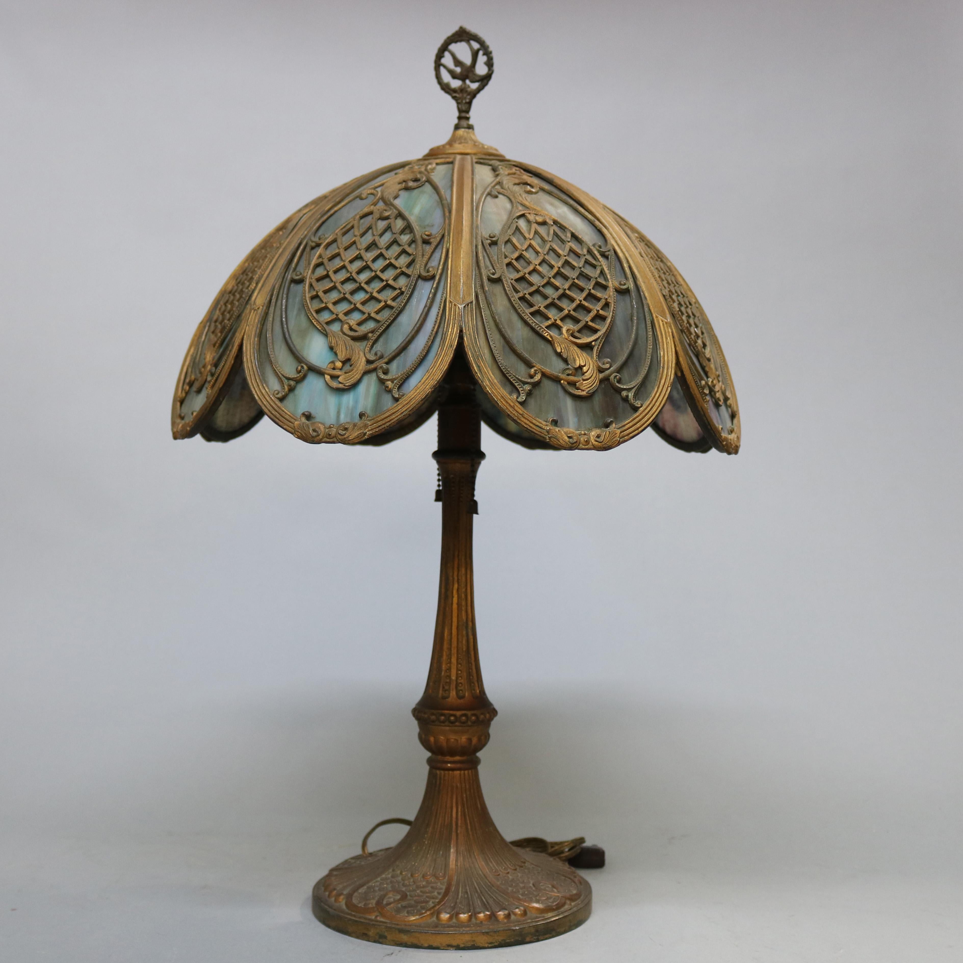 An antique Arts & Crafts Bradley and Hubbard table lamp offers dome shade with pierced filigree scroll, foliate and diamond patterned panels having bent slag glass and stylized bird finial, surmounting double socket base, circa 1920

Measures -