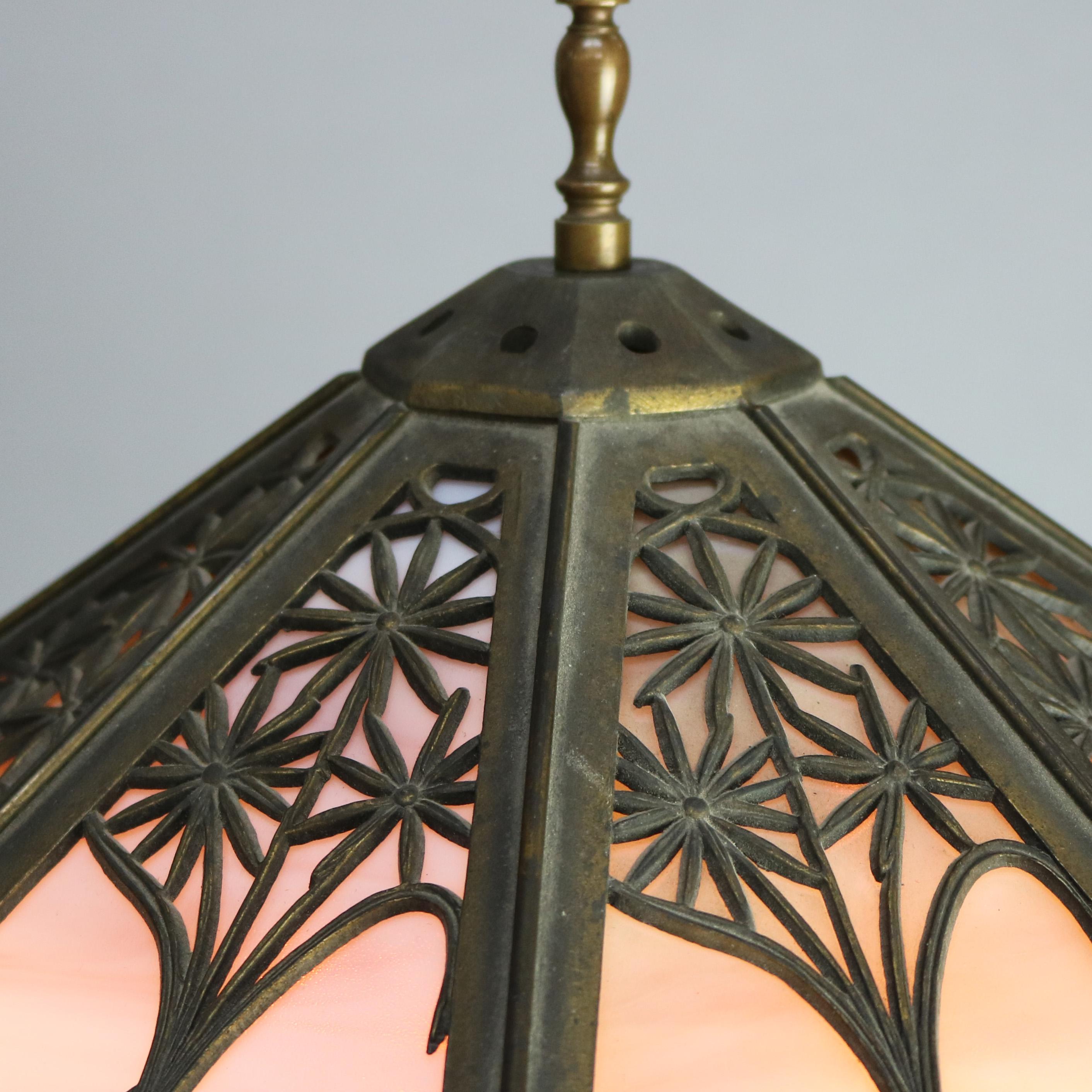 An antique Arts & Crafts table lamp by Bradley and Hubbard offers paneled slag glass shade with cast floral filigree shade housing tri-tone slag glass over foliate cast square base, signed B&H, circa 1920.

Measures: 23.75