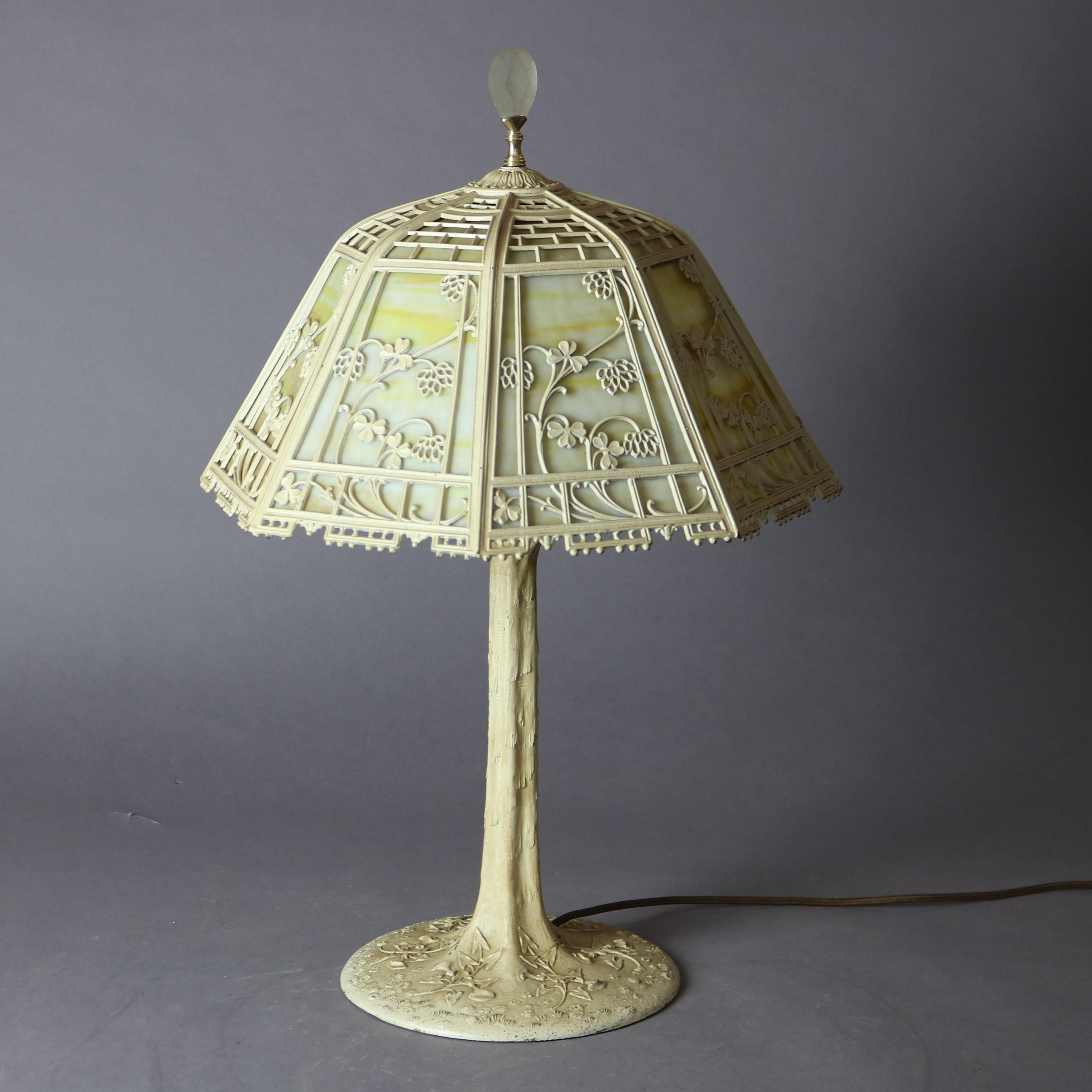 An antique Arts and Crafts Bradley and Hubbard table lamp offers dome form cast shade with floral elements and housing bent slag glass panels over triple 
 socket painted cast base, c1920

Measures - 23.5