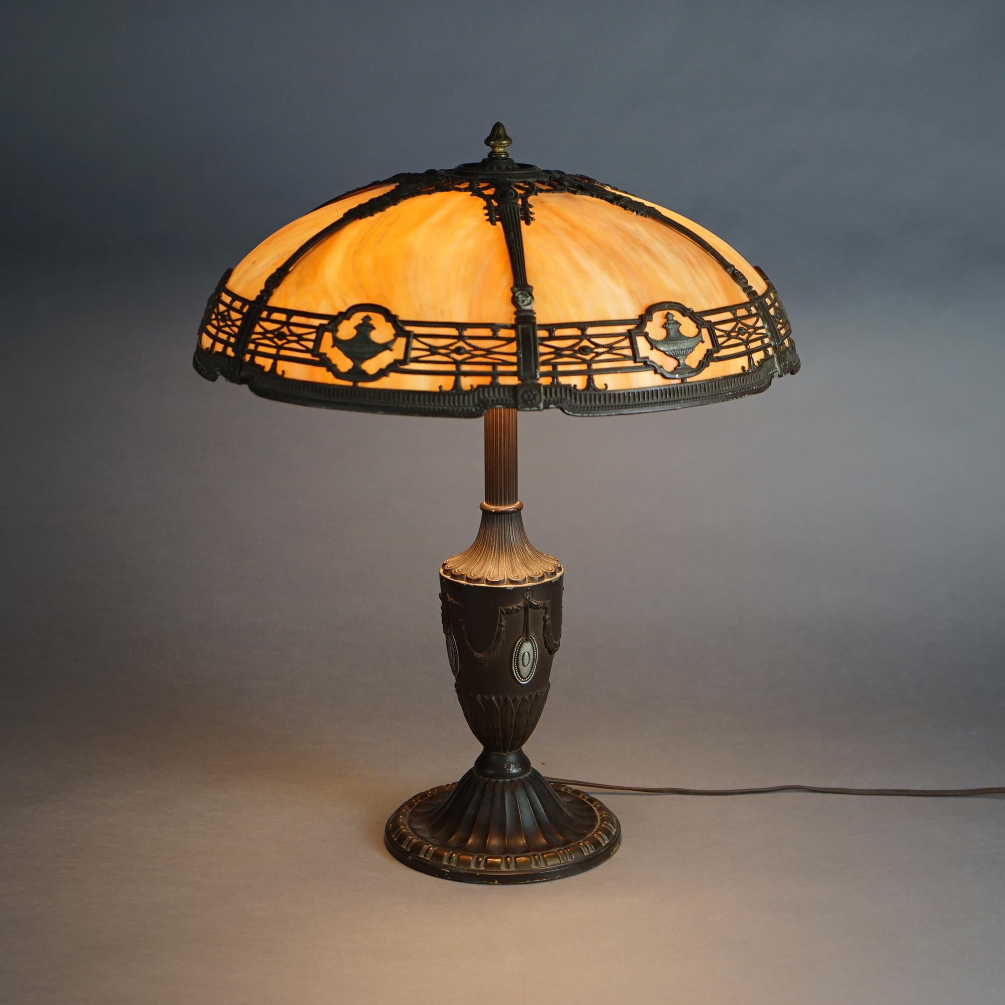 An antique Arts & Crafts table lamp by Bradley & Hubbard offers dome form cast shade having neoclassical elements and housing bent slag glass panels over cast urn form three light base, c1920
 
Measures- 22''H x 18.25''W x 18.25''D