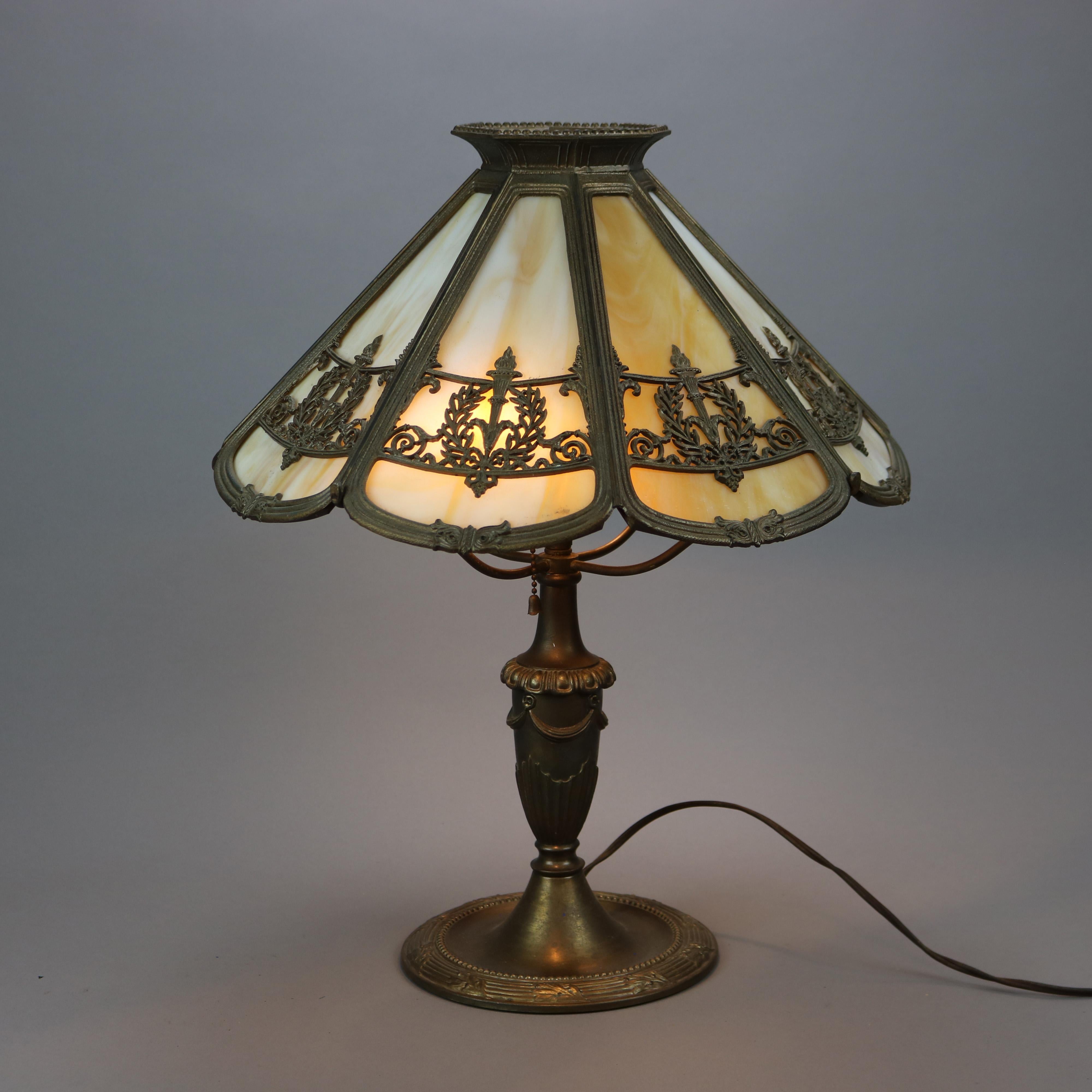 An antique Arts & Crafts table lamp by Bradley and Hubbard offers filigree cast shade having torch and laurel wreath Victory design housing slag glass panels over double socket cast base, signed on base as photographed, c1920

Measures - 20.5''h x