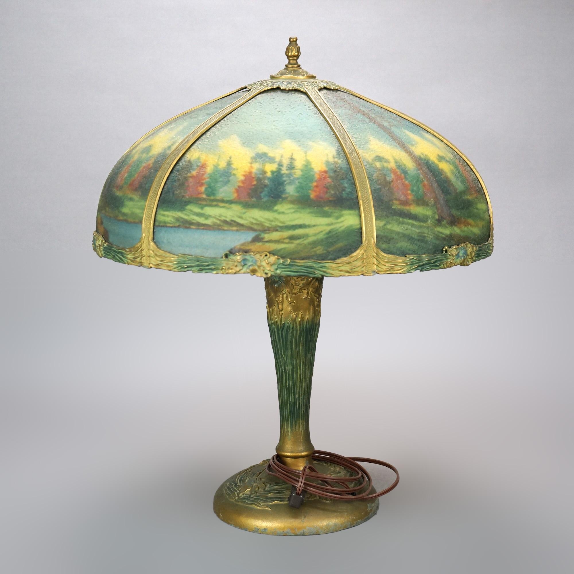 An antique Arts and Crafts table lamp in the manner of Bradley & Hubbard offers polychromed cast double socket base with matching shade housing six reverse painted bent glass panels having landscape lake scene, c1920

Measures - 22