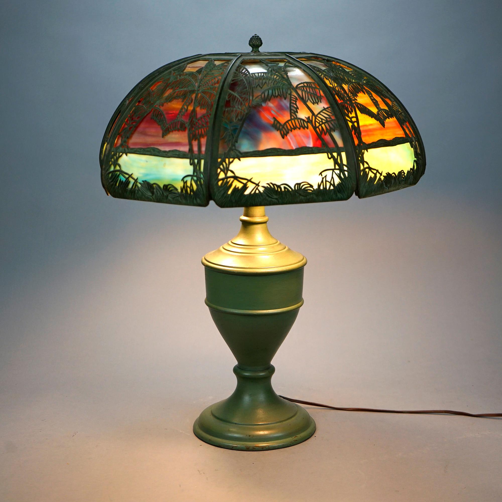 An antique Arts and Crafts table lamp by Bradley and Hubbard offers filigree cast dome form shade with palms housing two tone bent slag glass panels over double socket urn form base, c1920

Measures- 23.5'' H x 18'' W x 18'' D.