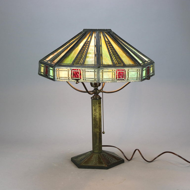 An antique Arts and Crafts table lamp by Bradley and Hubbard offers stylized feather cast paneled shade housing two-tone slag glass over single socket cast base, signed B&H as photographed, c1920

Measures - 19''H x 14.5''W x 14.5''D.