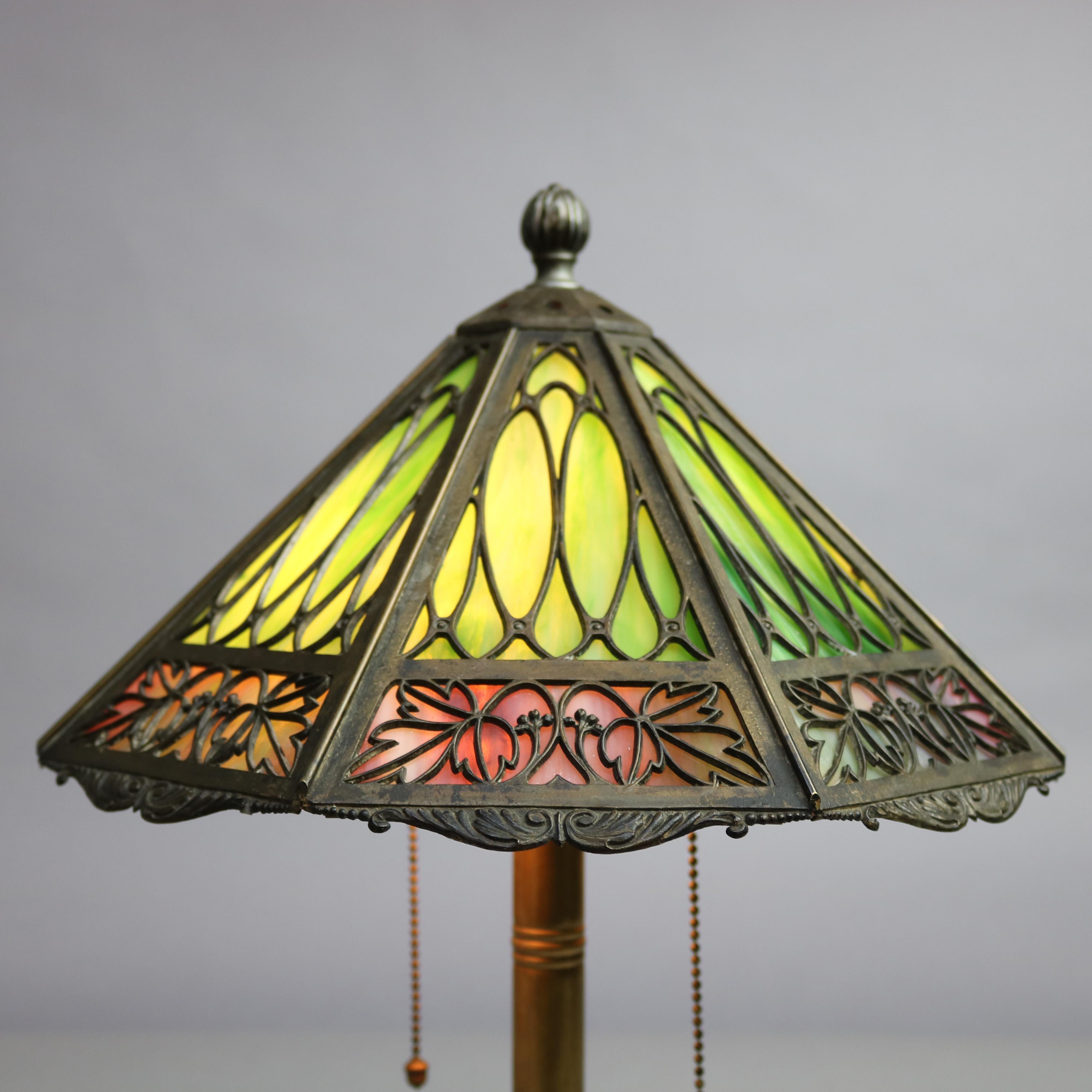 An antique Arts & Crafts table lamp by Bradley and Hubbard offers cast paneled shade frame with stylized foliate design and two-tone slag glass surmounting double socket base, stamped on base as photographed, circa 1920

Measures: 18.5