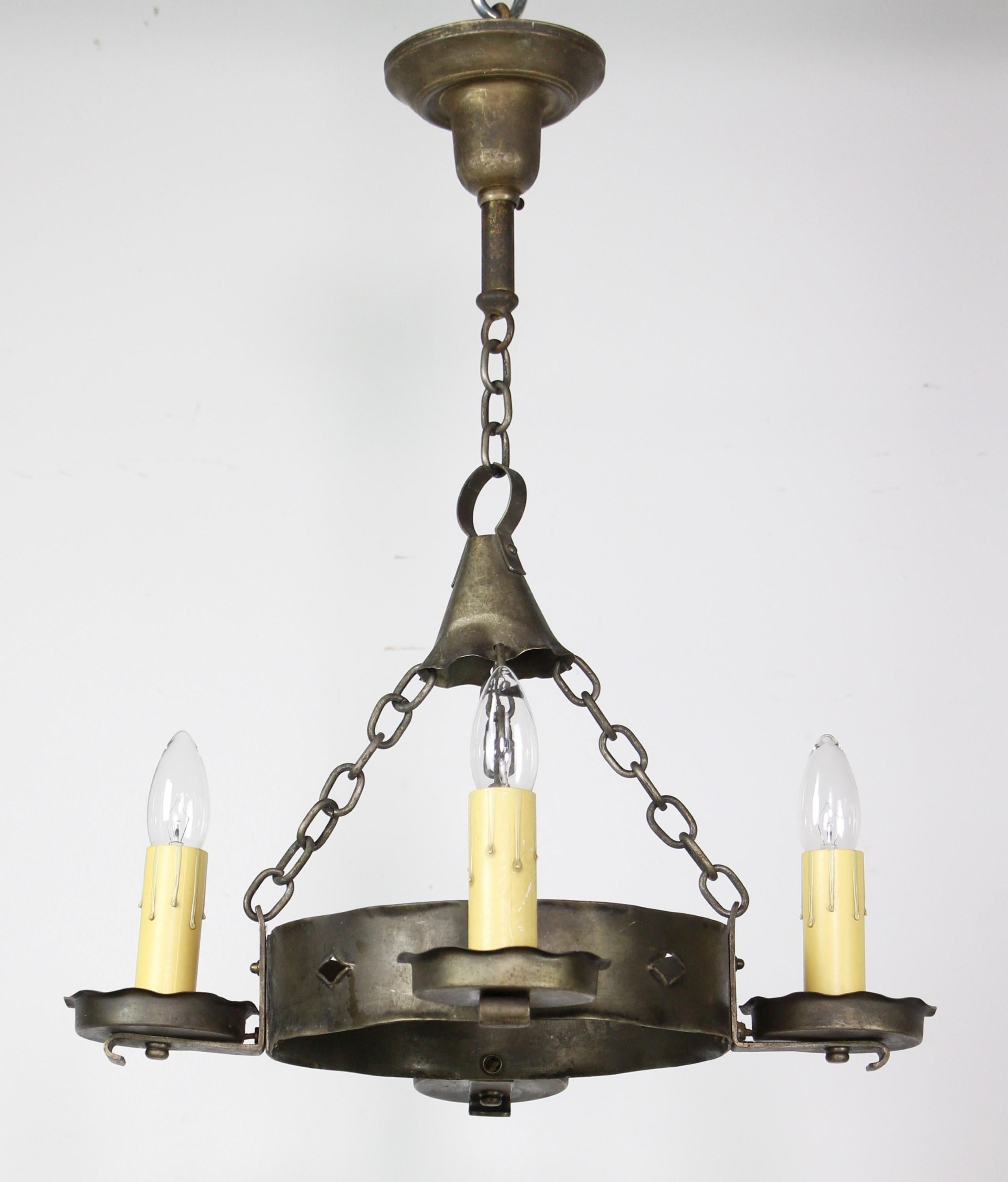 Early 1900s Arts & Crafts hammered brass chandelier with four candlestick arm lights.  This original chandelier has a round hammered wheel holding the 4 arms and is supported by a chain fitter.  The brass has a darkened patina.  The price includes