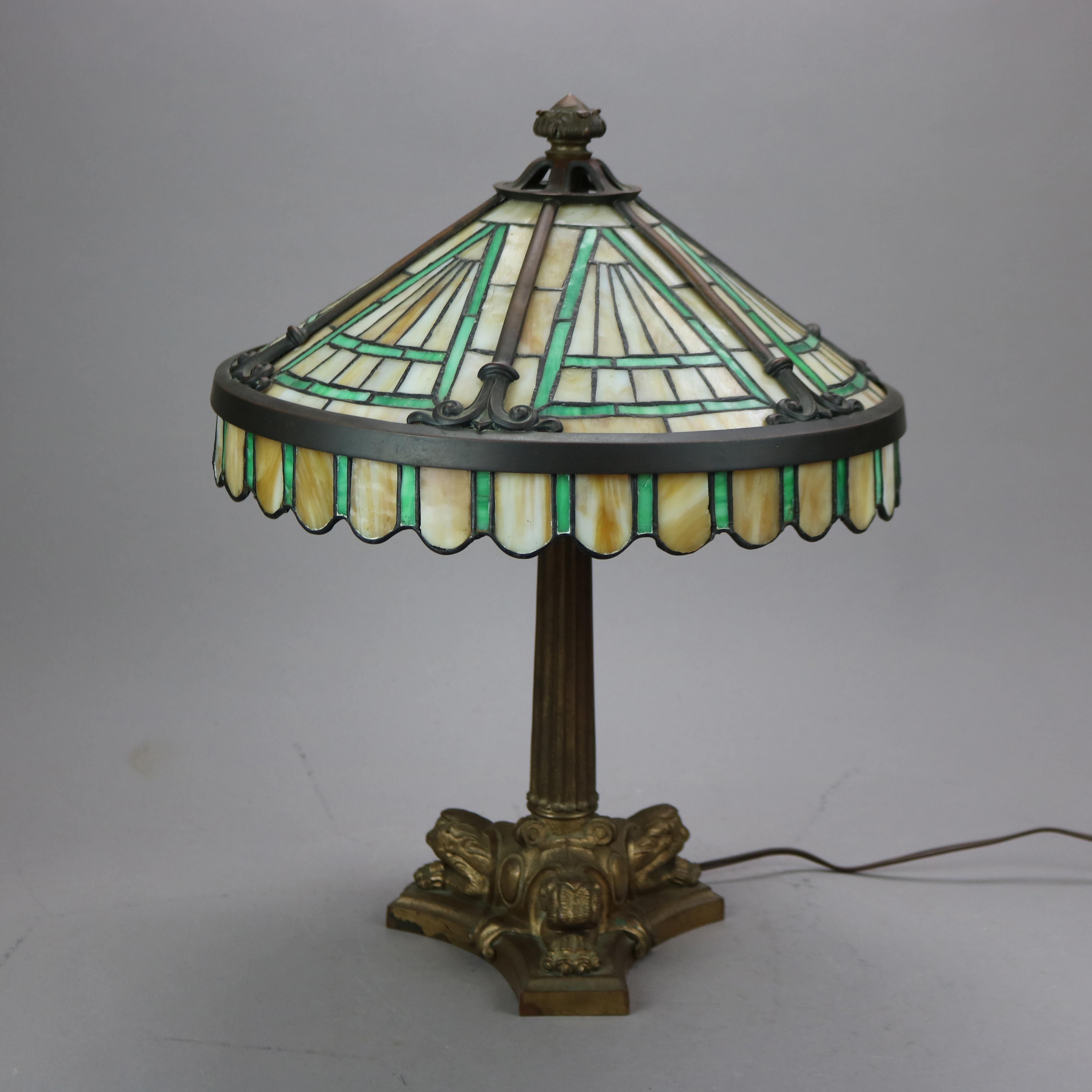 An antique Arts & Crafts table lamp in the manner of Duffner and Kimberly offers leaded glass shade with awning style apron on cast bronze triple socket base having flared and reeded column and paw feet, c1920

Measures- 19'' H x 14.5'' W x 14.5''