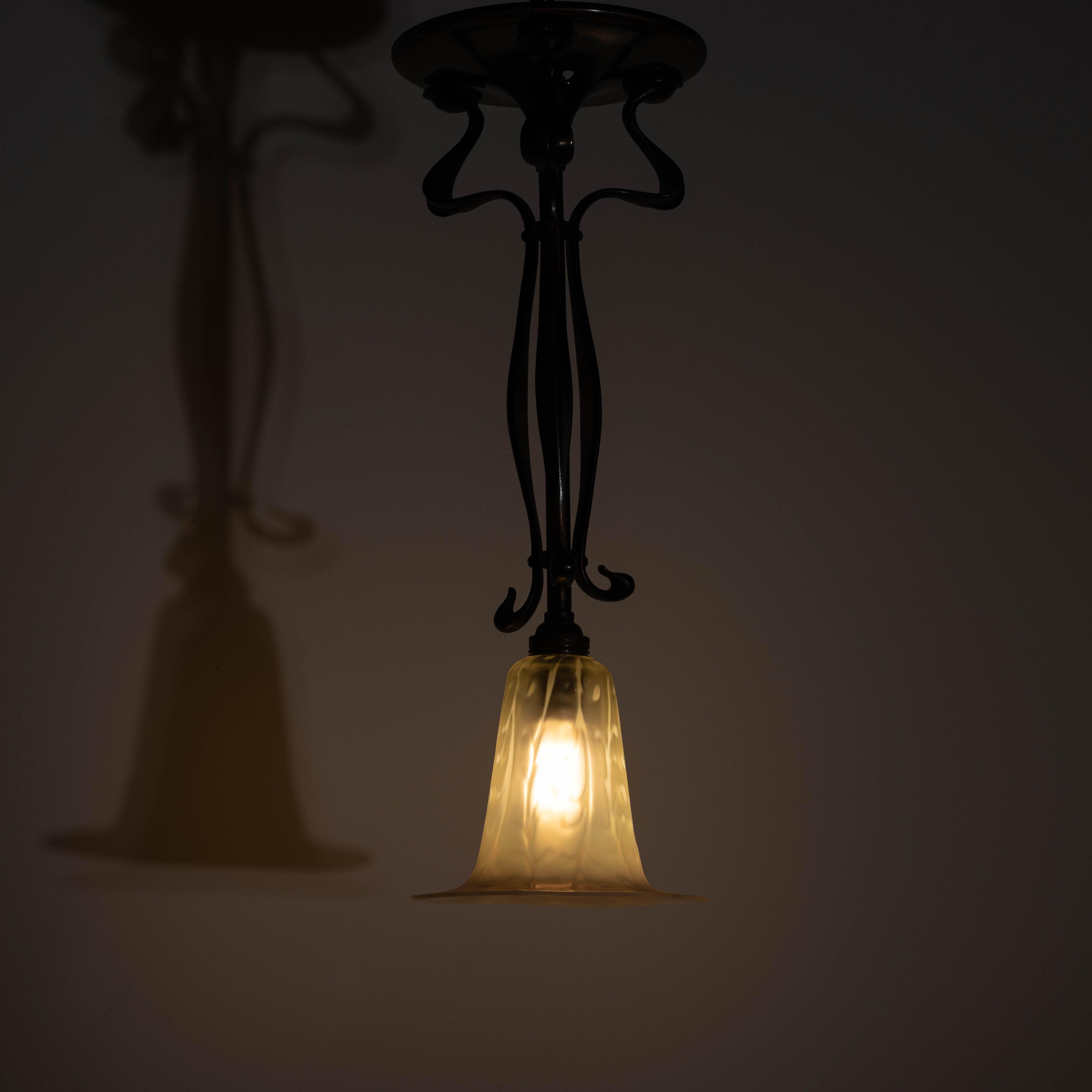 ANTIQUE ARTS & CRAFTS CAST COPPER FINISH LAMP WITH RARE STRAW VASELINE VEINED BELL FORM SHADE

A beautiful Arts & Crafts period lamp with a sculptural, organic frame in cast brass with an aged copper oxide finish. The sinuous form and hammered