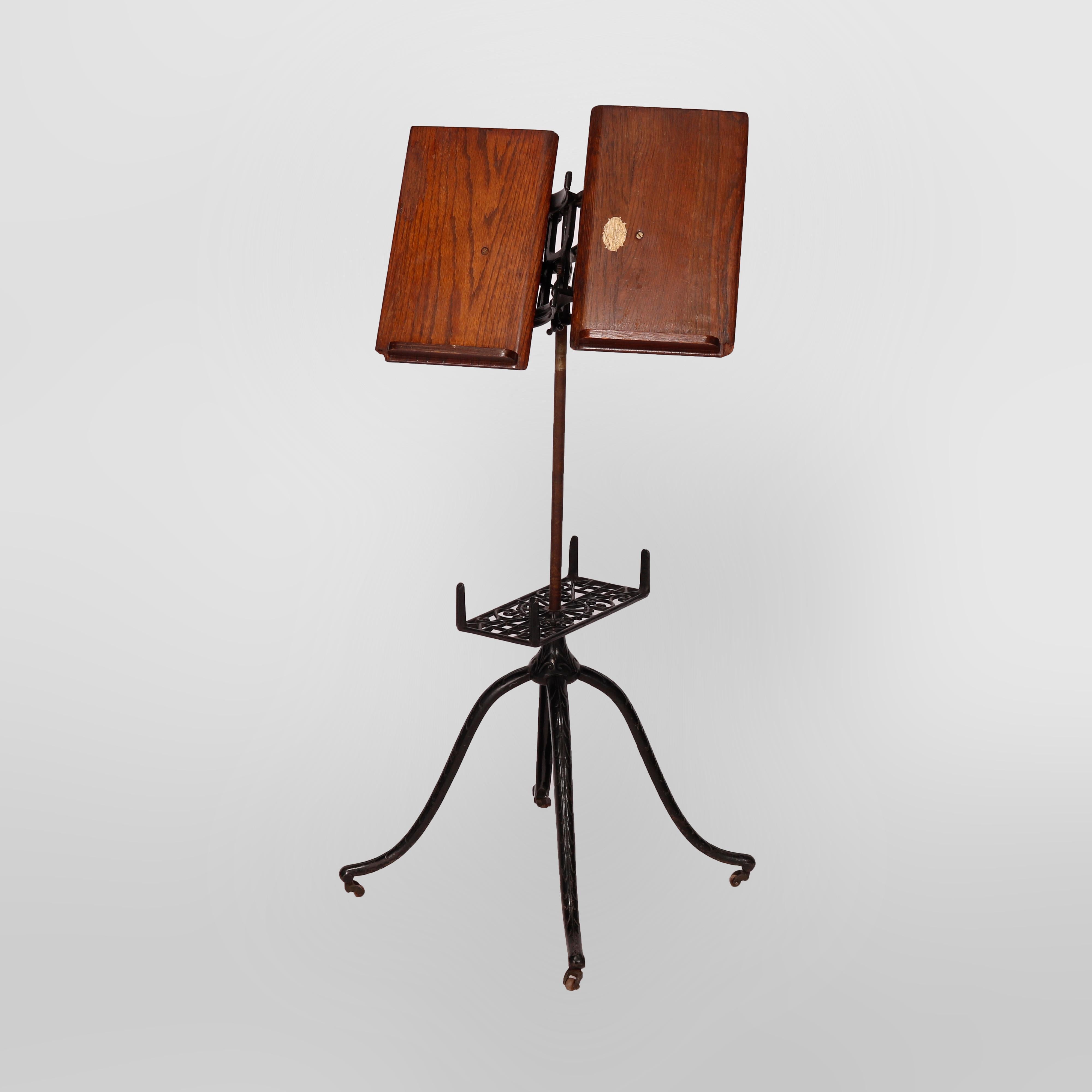 An antique Arts & Crafts library or parlor dictionary book stand by Columbia offers cast iron quadripod base with cabriole legs and pierced cast foliate lower shelf surmounted by adjustable display, seated on casters, maker label as photographed,
