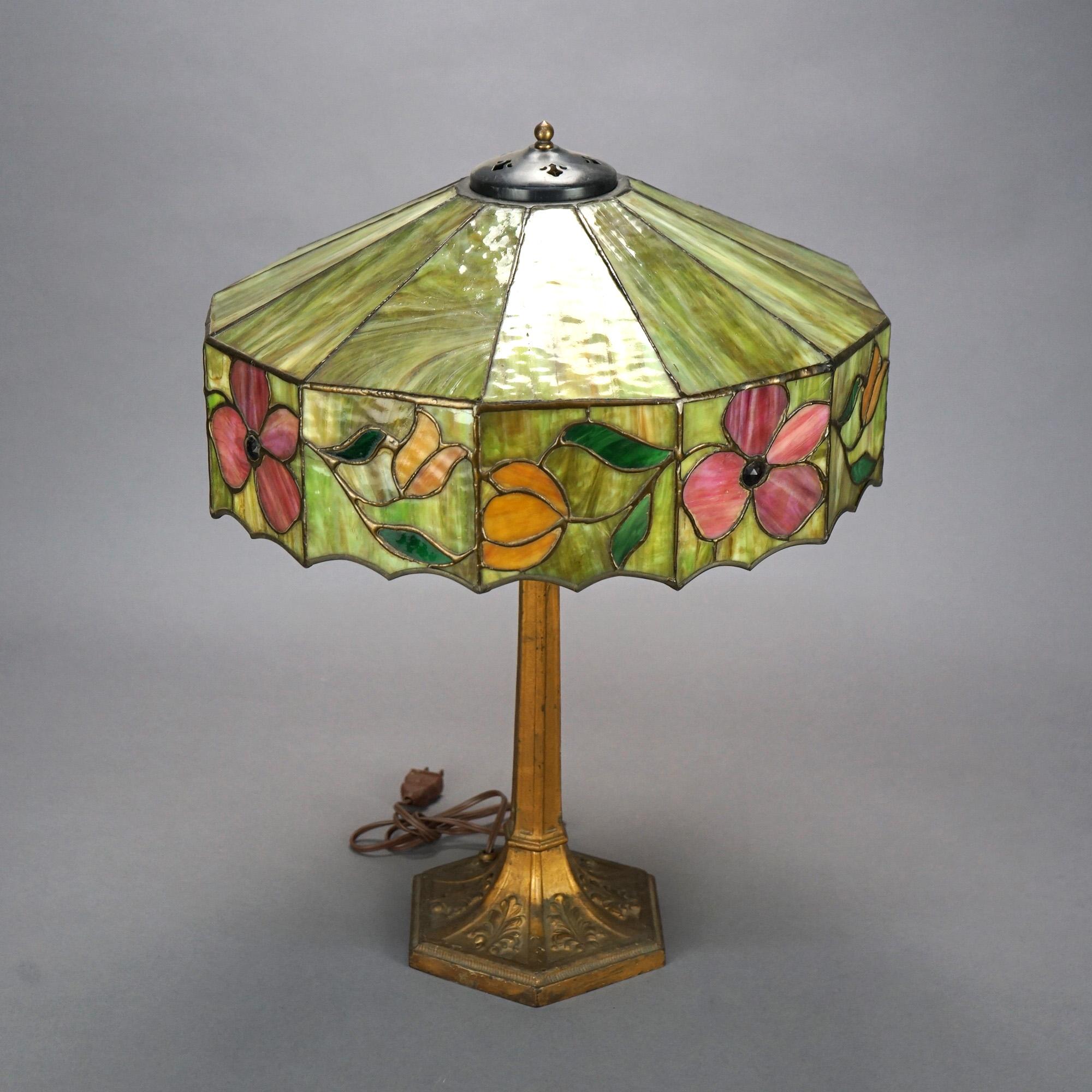 An antique Arts and Crafts table lamp offers leaded slag and jeweled glass shade with floral and scalloped rim over double socket cast base, c1920.

Measures- 22.75'' H x 17.25'' W x 17.25'' D.