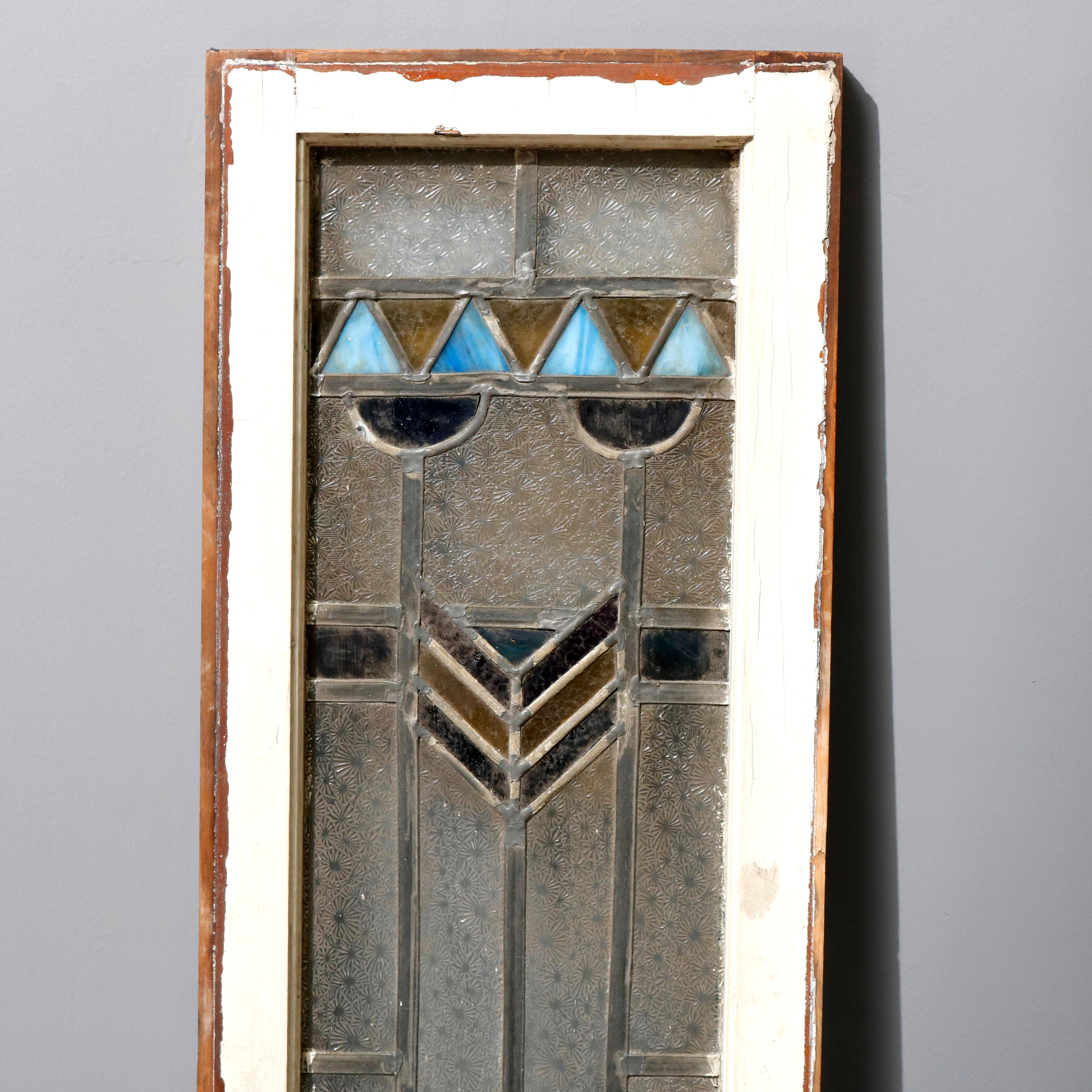 A pair of Arts & Crafts Frank Lloyd Wright style window panels each offers leaded stained glass in geometric form and having central stylized feather and floral patterns, encased in wood window sash, circa 1910

Measures: 54