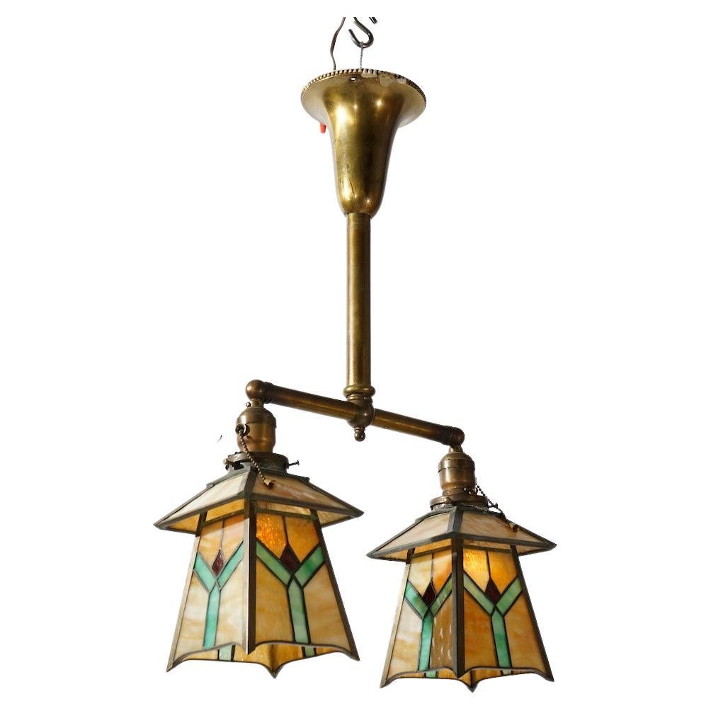 An antique Arts and Crafts Frank Lloyd Wright Prairie School chandelier offers frame with single column having double arms, each terminating in drop lights with leaded glass shades with geometrical design, c1920

Measures- 26''H x 15.25''W x 5.5''D