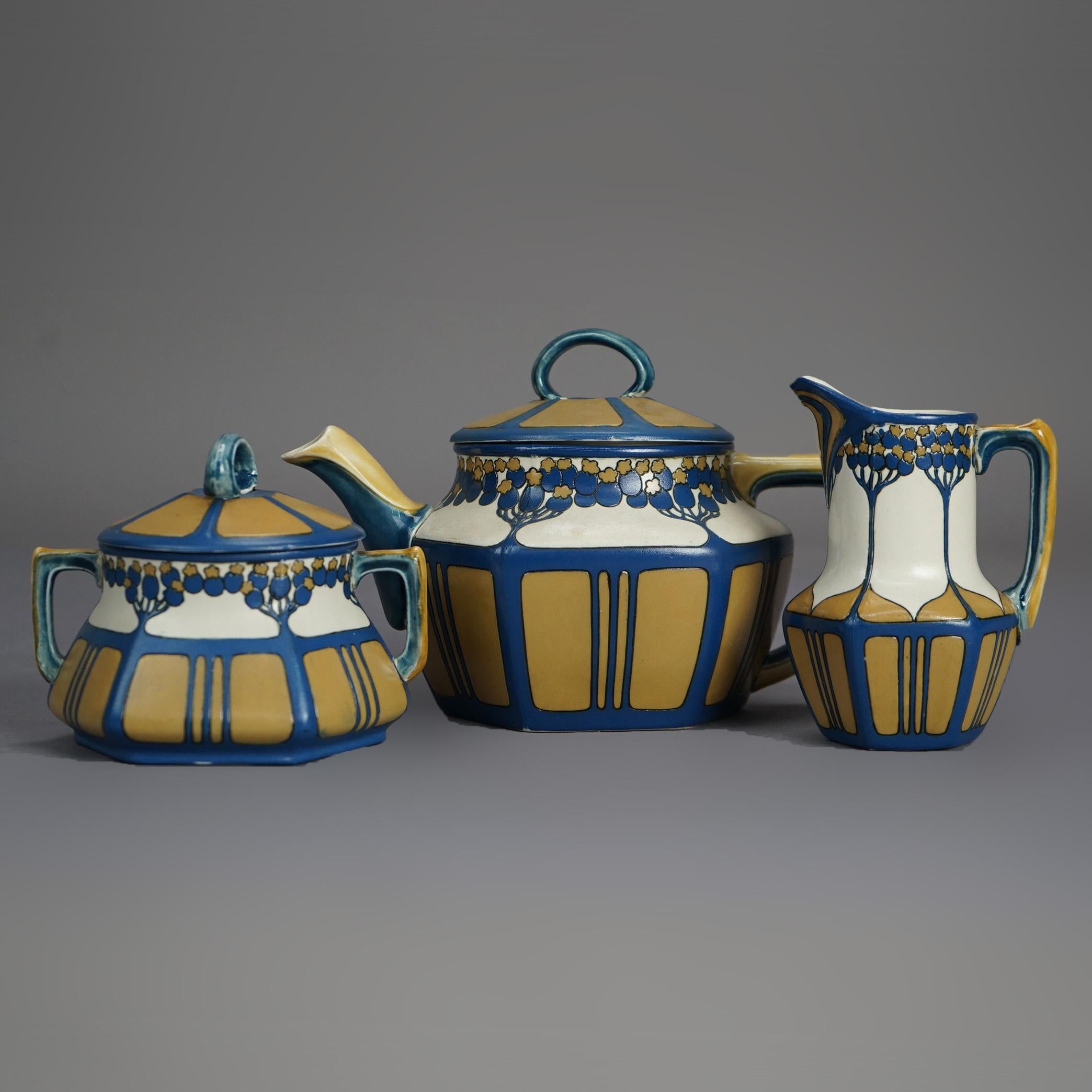 An antique Arts & Crafts German Mettlach pottery tea set in faceted form with hand painted tree design; set includes tea pot, covered sugar and creamer; signed on bases as photographed; 20th century.

Measures- Pitcher: 4.75''H x 2.75''W x 3.25''D;