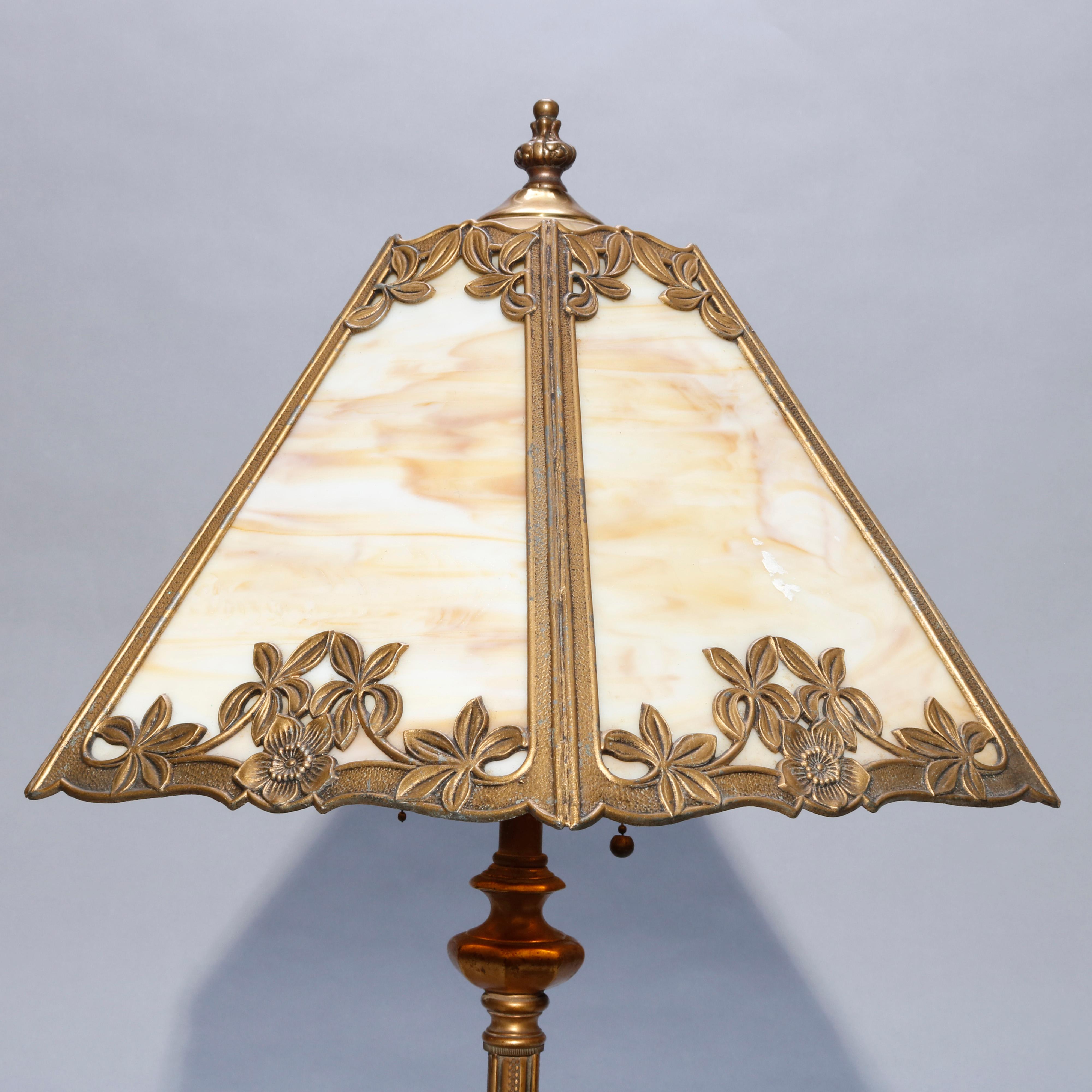 An antique Arts & Crafts table lamp in the manner of Bradley & Hubbard offers cast paneled shade with floral elements housing slag glass panels and surmounting double socket gilt base, circa 1920

Measures- 24