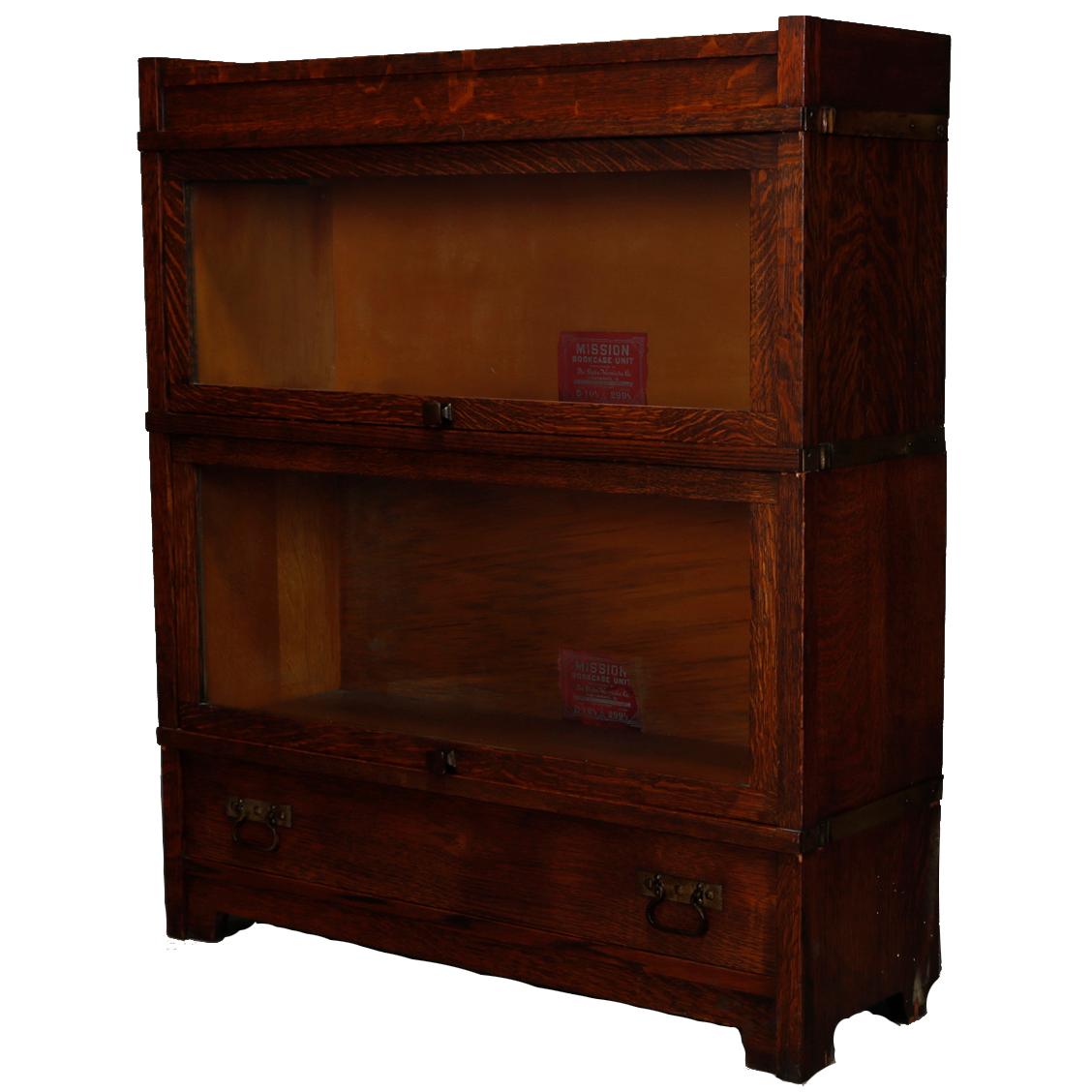 An antique Arts & Crafts Mission Barrister bookcase by Globe Wernicke offers quarter sawn oak construction with two stacks having pull out glass doors over lower long drawer with cast pulls raised on squared legs, circa 1910.

Measures: 40