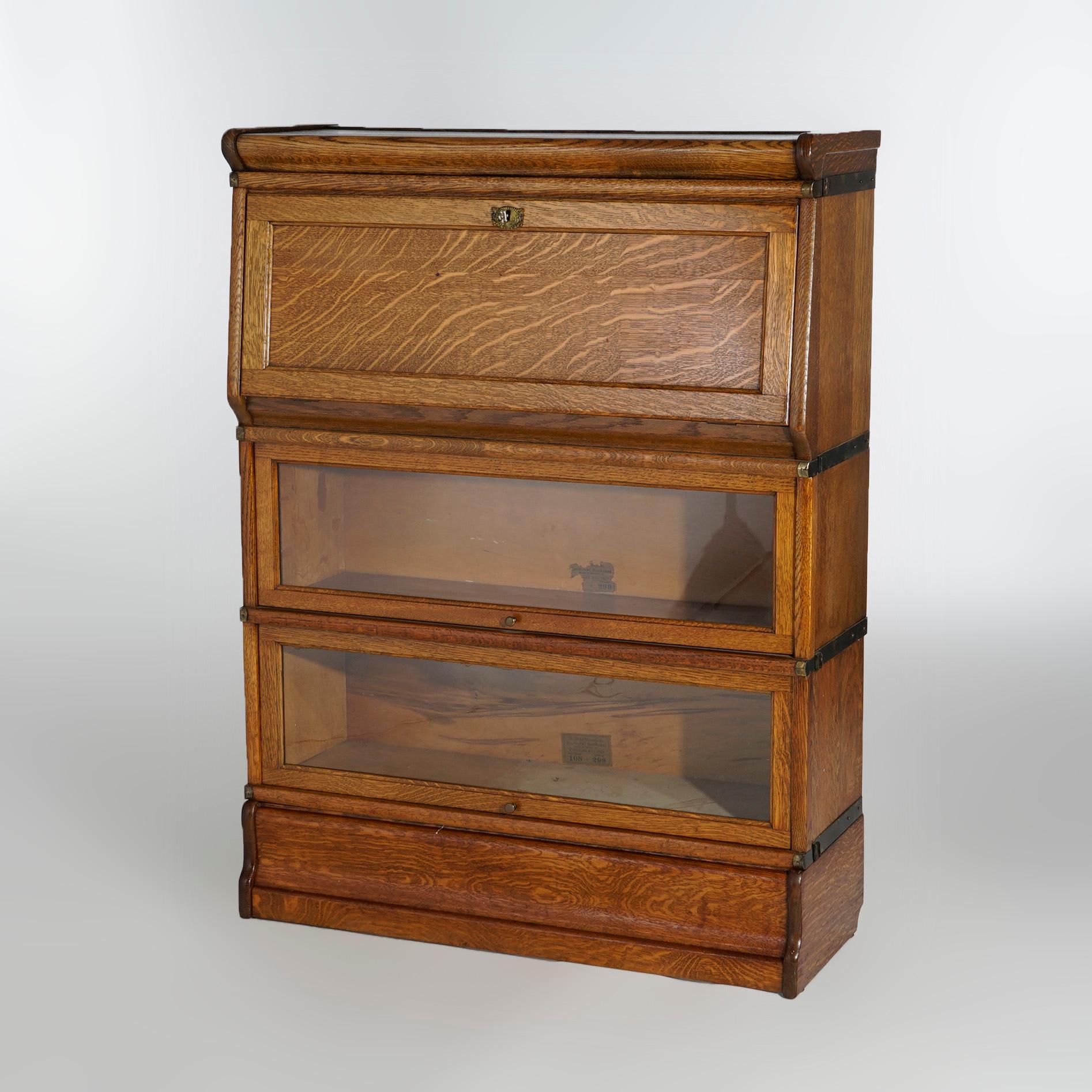 An antique Arts and Crafts barrister secretary bookcase by Globe Wernicke offers quarter sawn oak construction with upper stack having drop down desk opening to interior with storage compartments, over two stacks with pullout glass doors, raised on