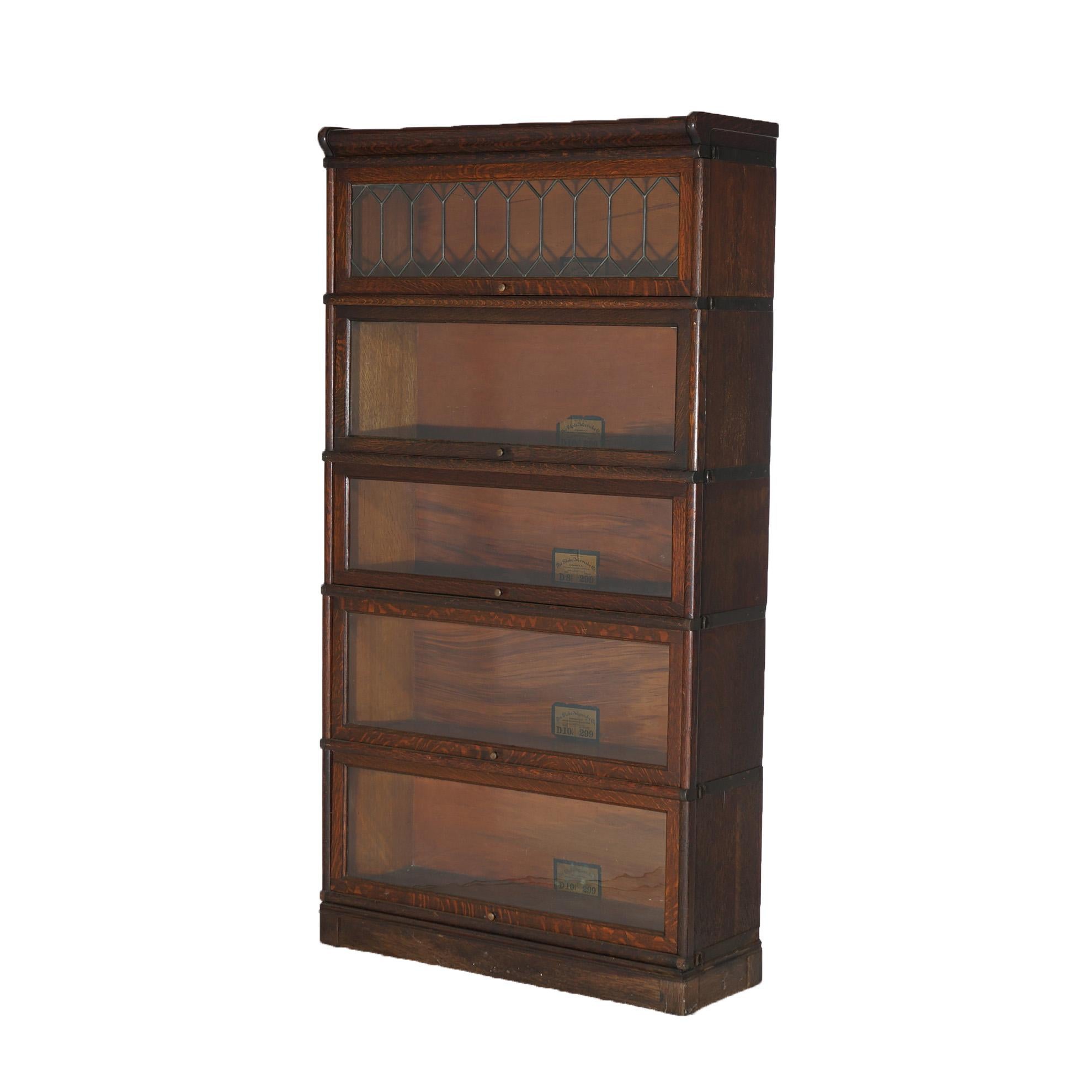 An antique Arts and Crafts barrister bookcase by Globe Wernicke offers quarter sawn oak construction with five stacks, each having pullout glass doors including one with leaded glass, and raised on square straight base, maker labels as photographed,