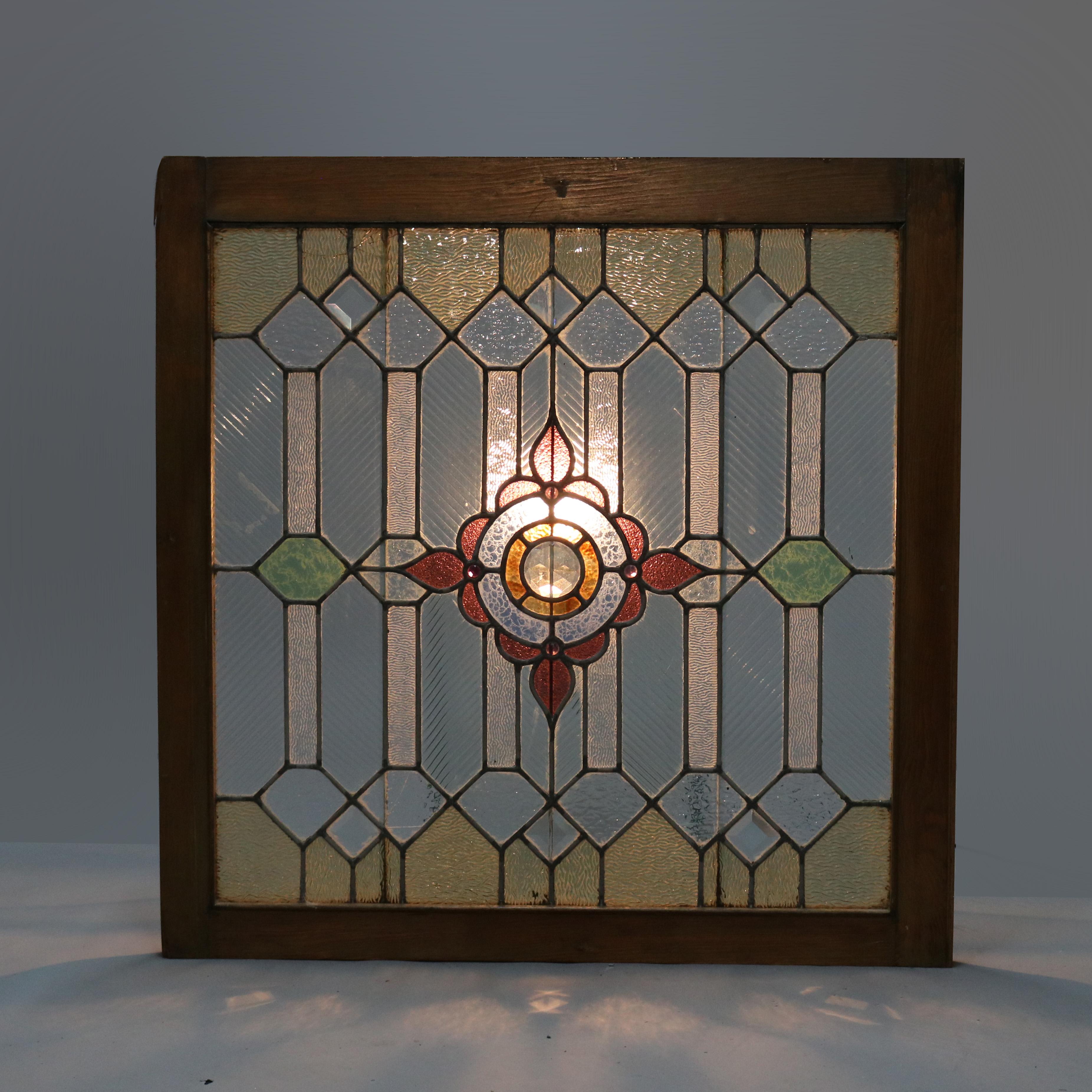 An antique Arts & Crafts windows offers leaded jeweled and stained glass with central stylized foliate medallion element, seated in wood sash, c1910

Measures: 35