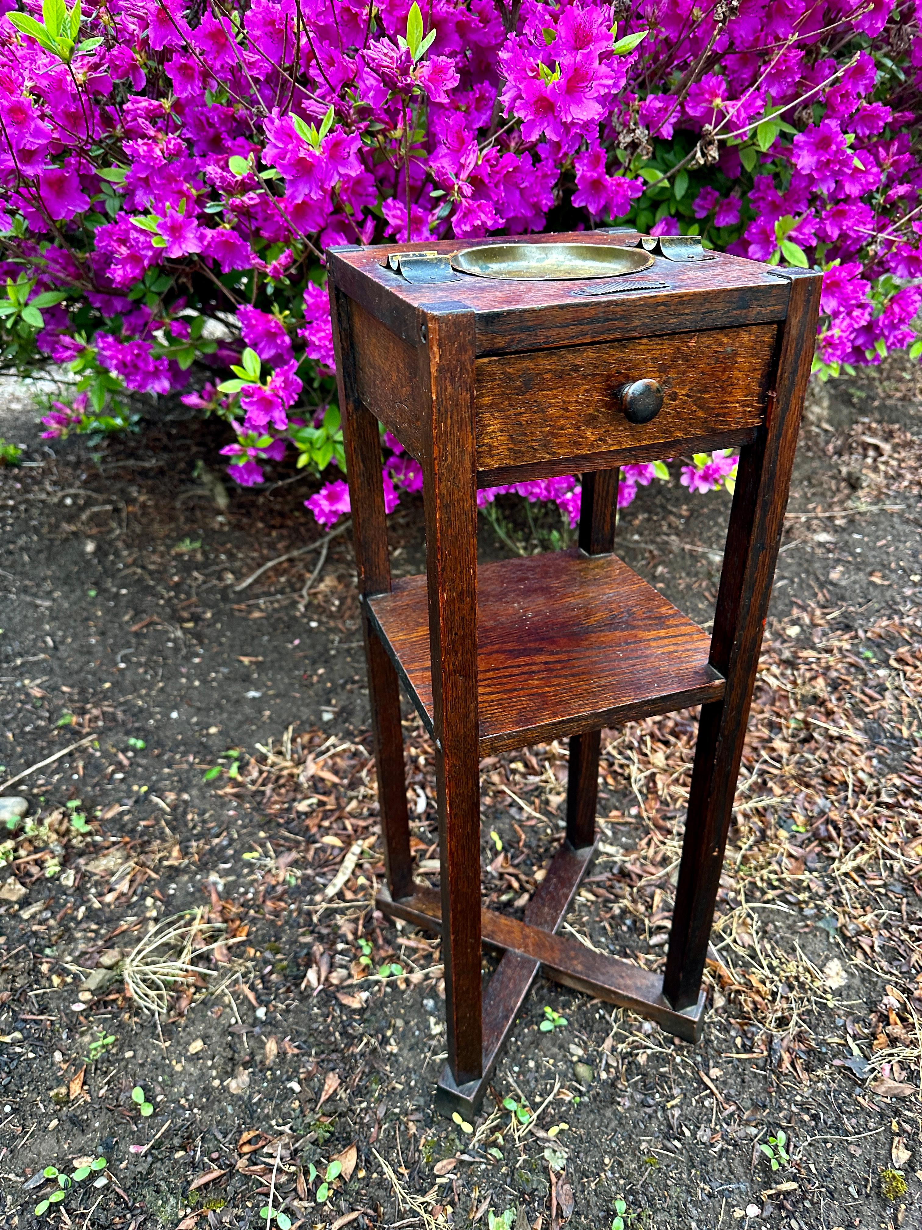 Se trata de un Antiguo Soporte para Fumar Pequeño Kushman Arts & Crafts con cajón.  Incluye un cenicero de latón y dos portapuros de latón en la parte superior del soporte. La parte inferior tiene un diseño de zapato-pie.  ¡ROBUSTO Y FUERTE! Está