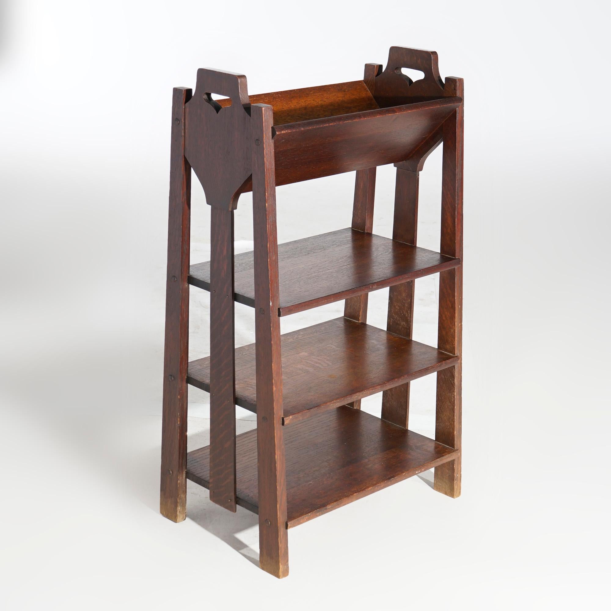 An antique Arts and Crafts bookshelf by Lakeside Crafters offers quarter sawn oak construction in tapered form with slat sides, upper book cradle over lower graduated shelves, maker label as photographed, c1910

Measures- 32.5'' H x 18.5'' W x