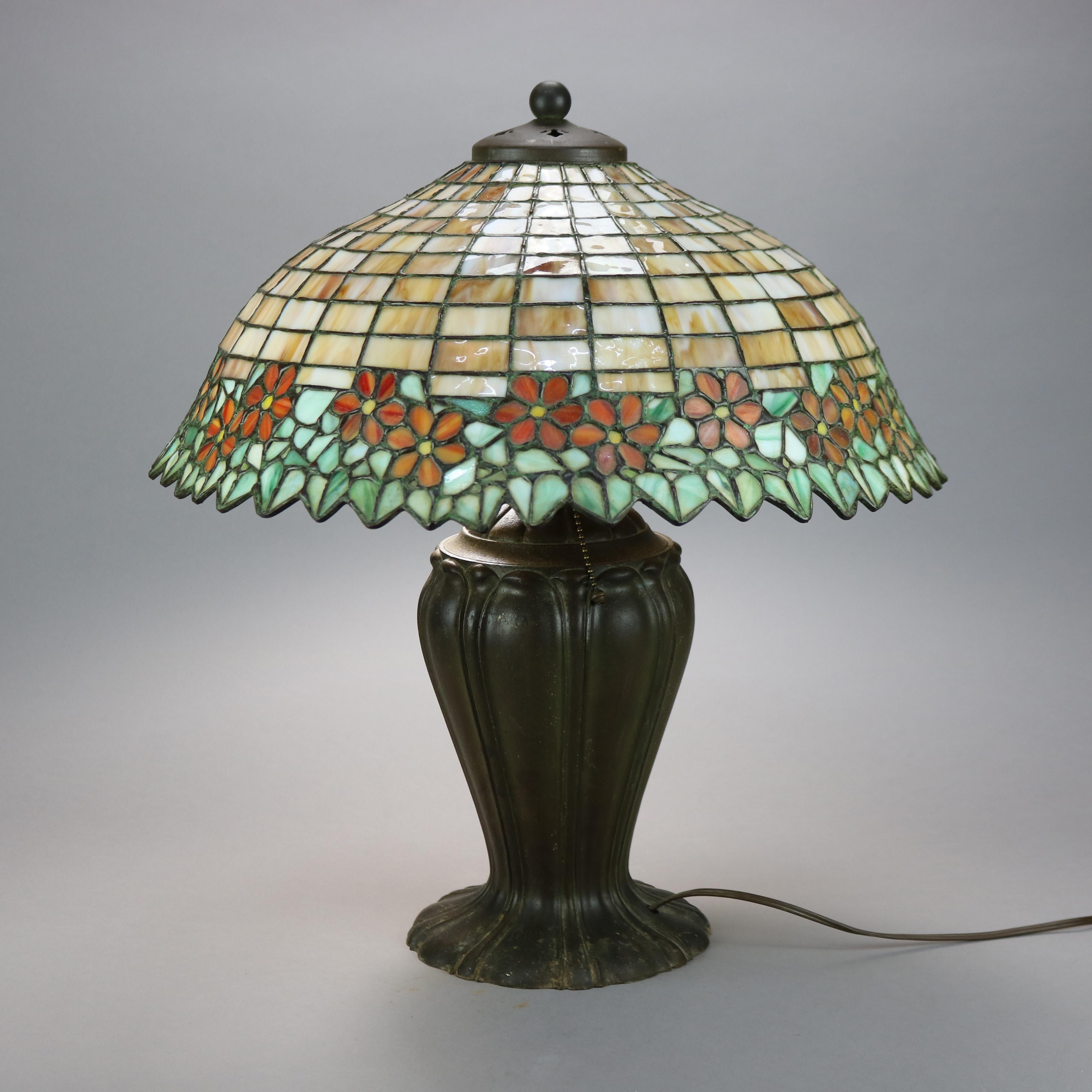 An antique Arts & Crafts table lamp offers leaded slag glass dome form shade having band of flowers attr. to Unique over cast urn form triple socket base attr. Handel, c1920

Measures - 21'' H x 19'' W x 19'' D.