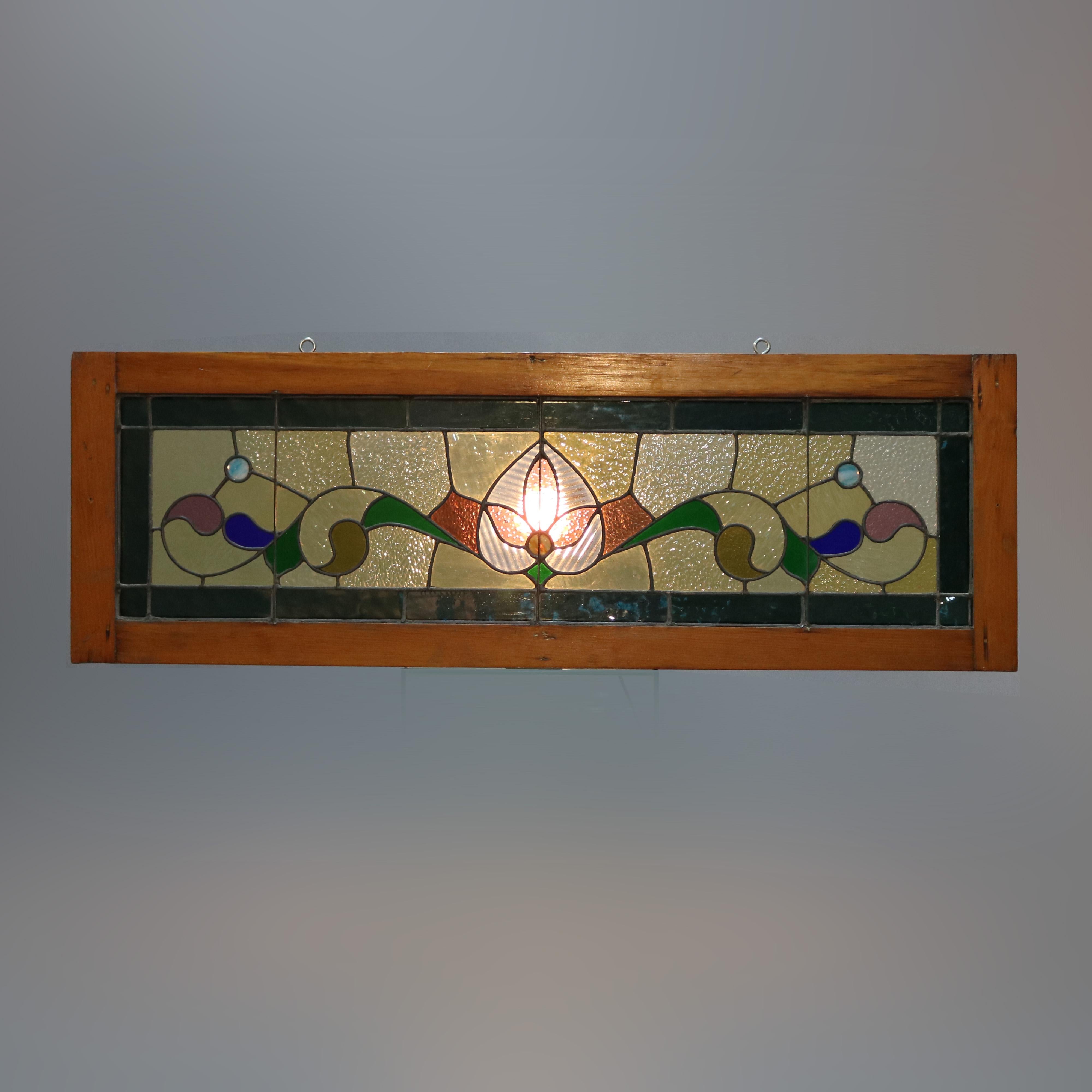 An antique Arts & Crafts long window offers leaded jeweled and stained glass with central foliate element with flanking scroll work, seated in wood sash, c1910

Measures: 17