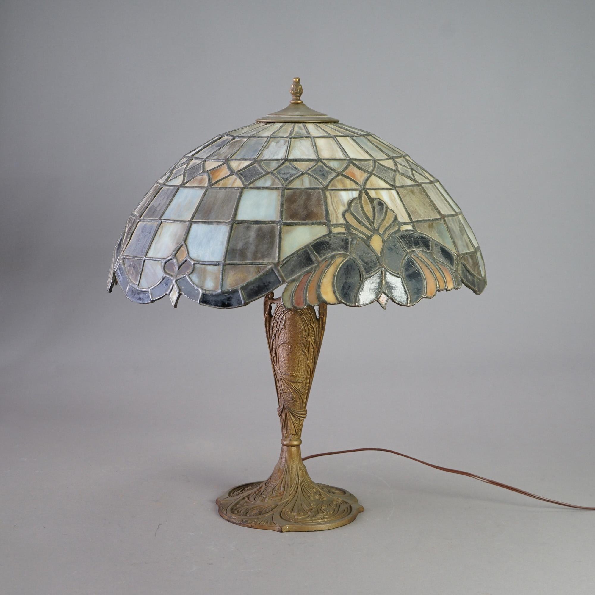 An antique Arts and Crafts table lamp offers leaded stained and slag glass dome-form shade with stylized foliate design over double socket cast base, c1920

Measures - 23