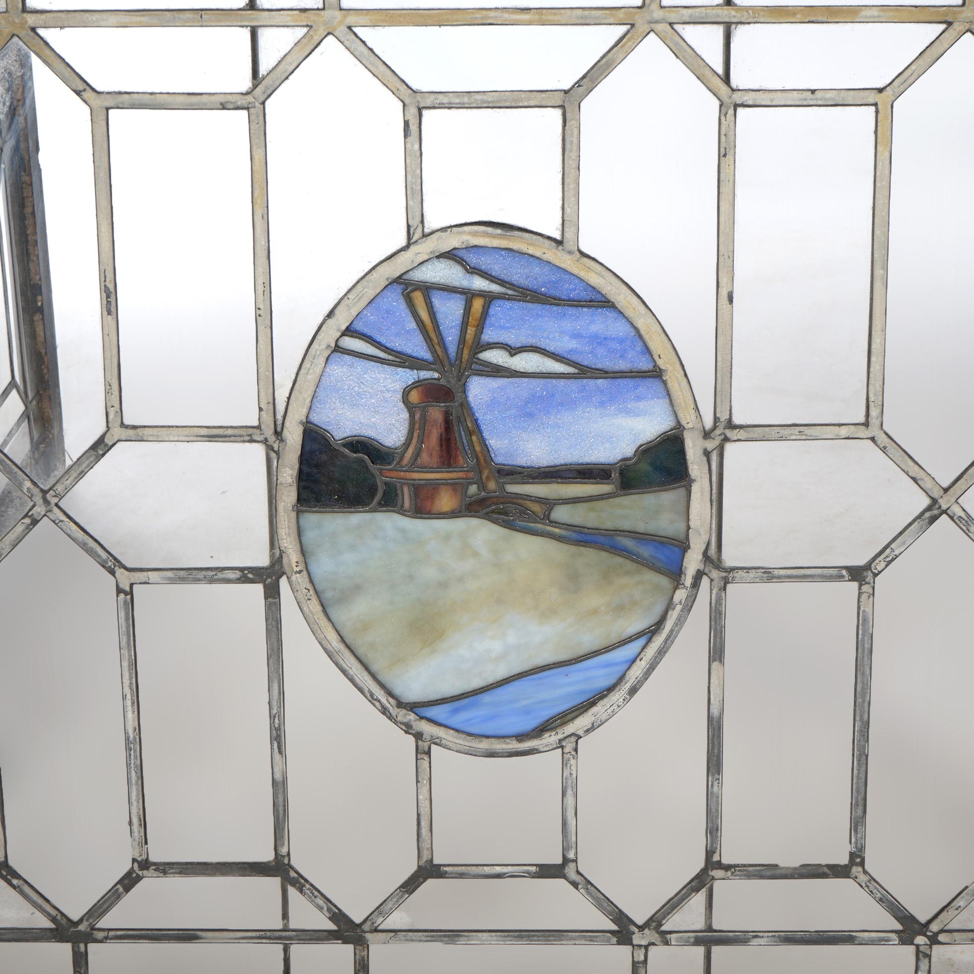 Ein antikes Arts & Crafts-Fenster bietet eine Bleiverglasung mit farblosen Paneelen, die eine zentrale Reserve mit einer Windmühle in ländlicher Umgebung umgeben, die in einem Holzflügel sitzt, um 1910

Maße - 32 