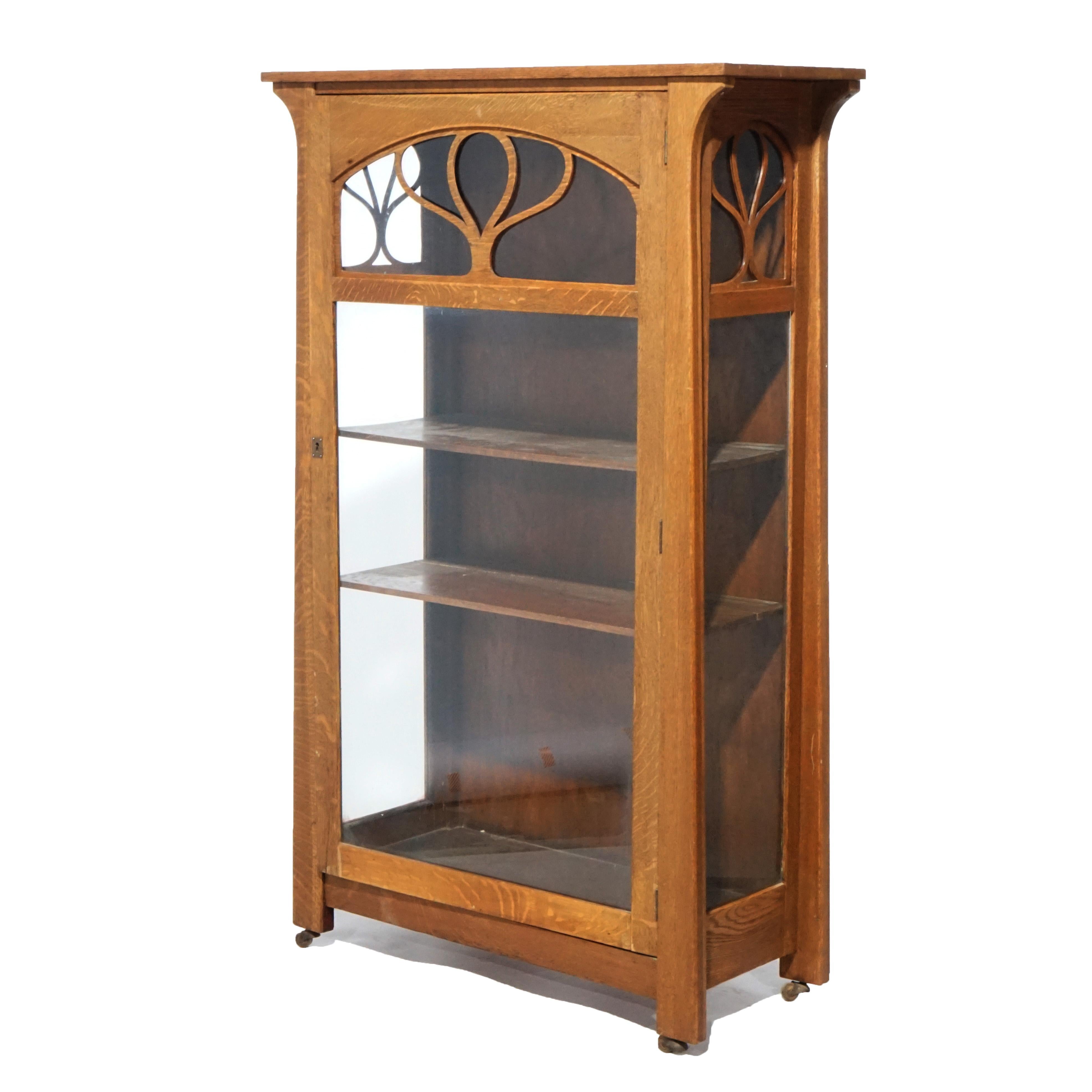 An antique Arts and Crafts china cabinet in the manner of Limbert offers quarter sawn oak construction with single glass door having filigree stylized tree and opening to shelved interior, raised on square and straight legs, c1910.

Measures-