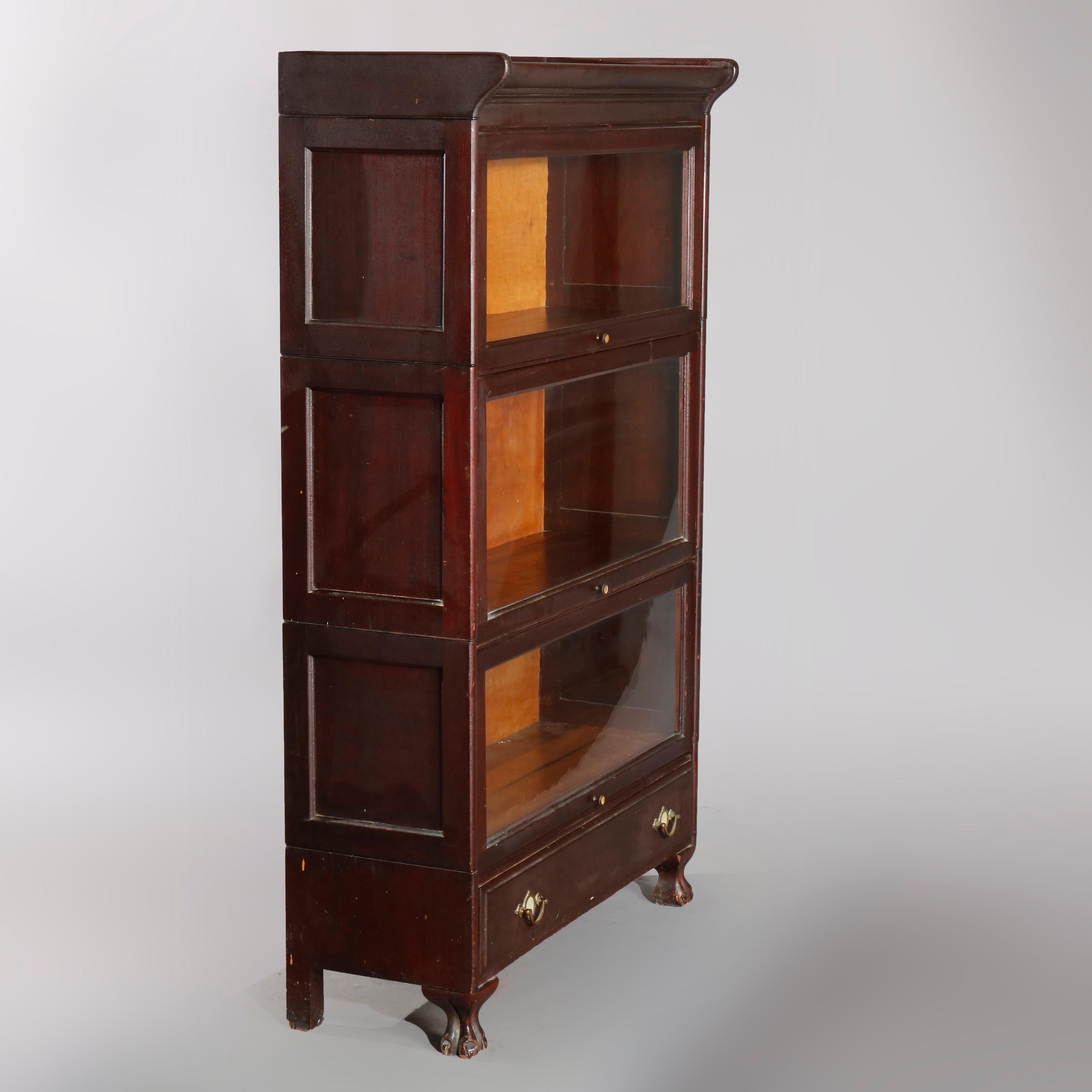 An Arts & Crafts sectional Barrister bookcase made in Grand Rapids offers mahogany construction with three stacks having a pull-down glass door on base with drawer having brass pulls with mother of pearl inlaid medallion and raised on cabriole legs