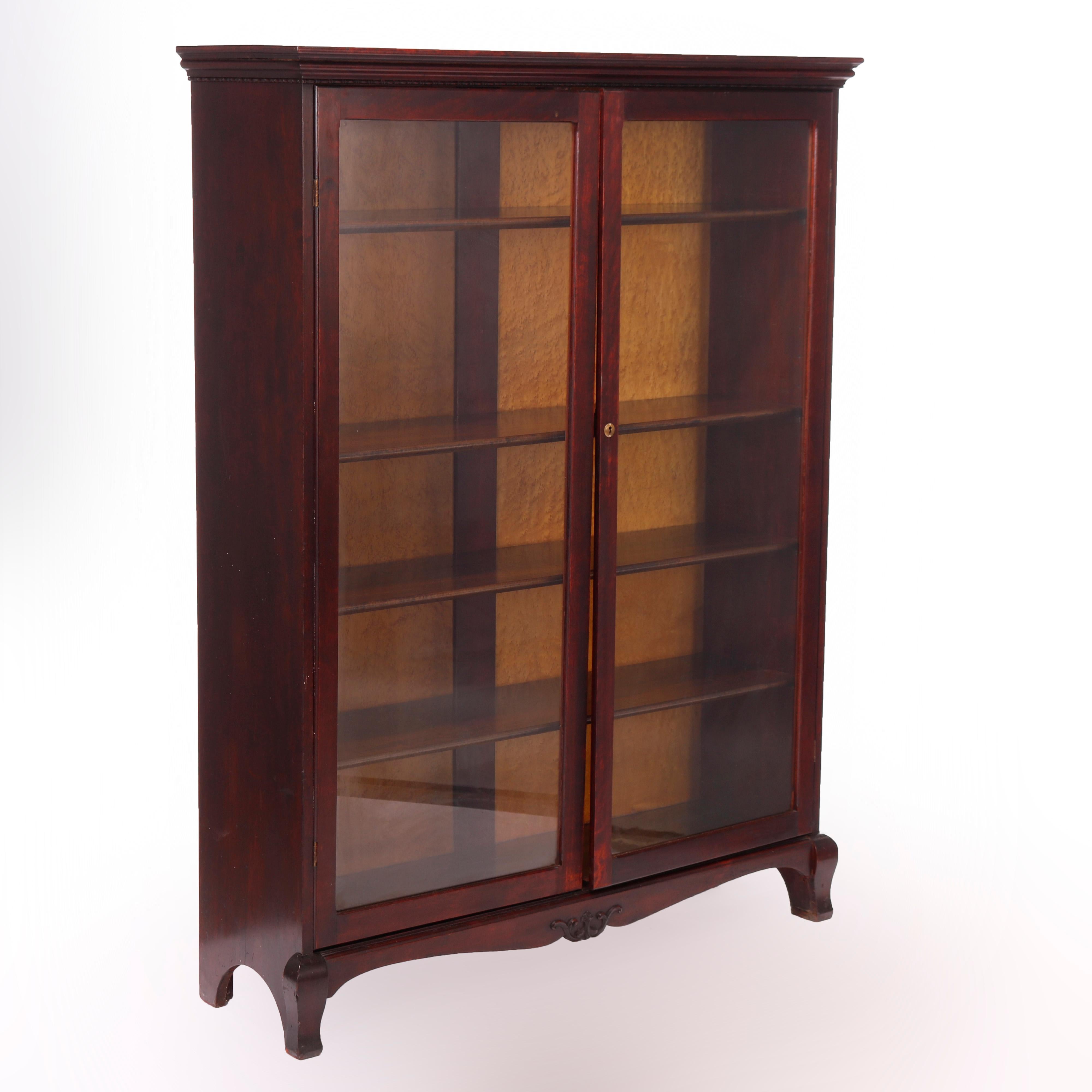 An antique Arts and Crafts bookcase offers mahogany construction with double glass doors opening to adjustable shelf interior over shaped skirt having central carved foliate element, raised on stylized cabriole legs, c1910

Measures - 60''H x