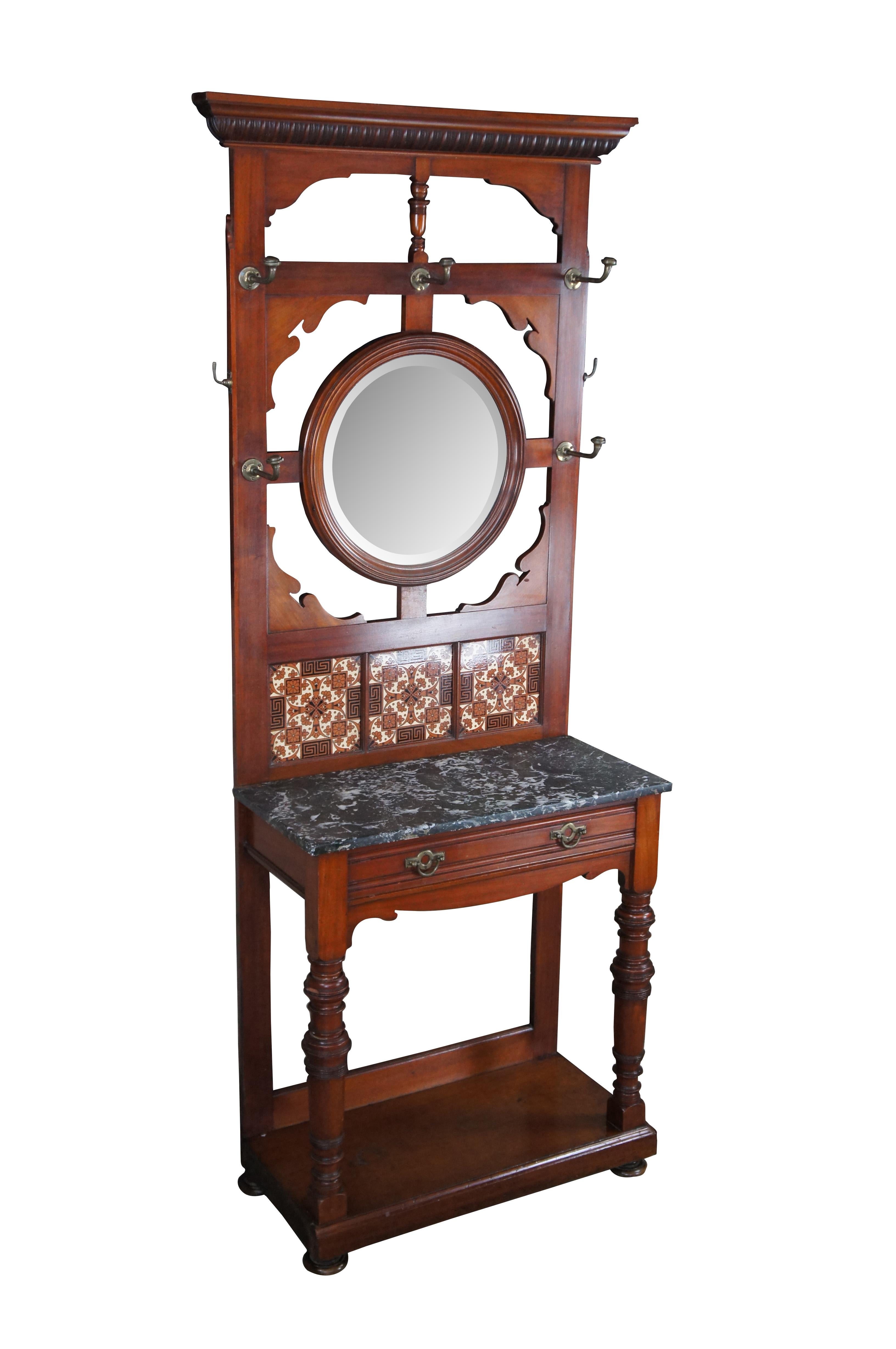 Antique Victorian era hall tree / stand / console.  Made of mahogany featuring arts and crafts styling with serpentine reticulated back supporting a round beveled mirror surrounded by multiple hooks / hangers.  The back features three tiled inserts,