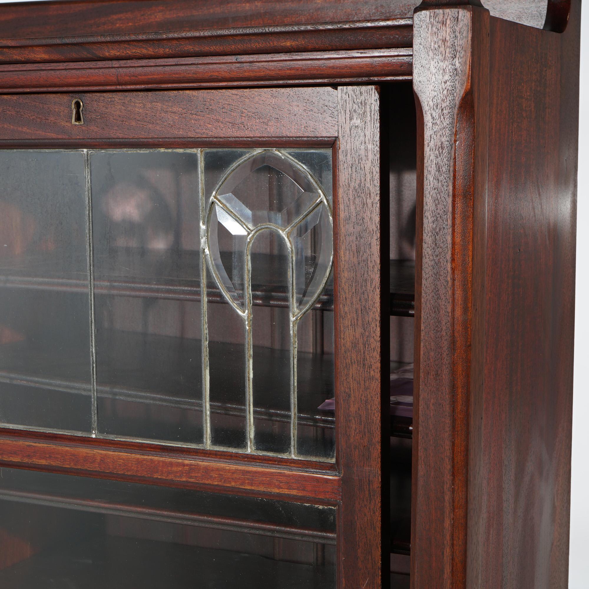An antique bookcase offers mahogany construction with upper gallery over case having sliding doors with leaded beveled glass in a stylized floral design, and opening to shelved interior, c1910

Measures - 57